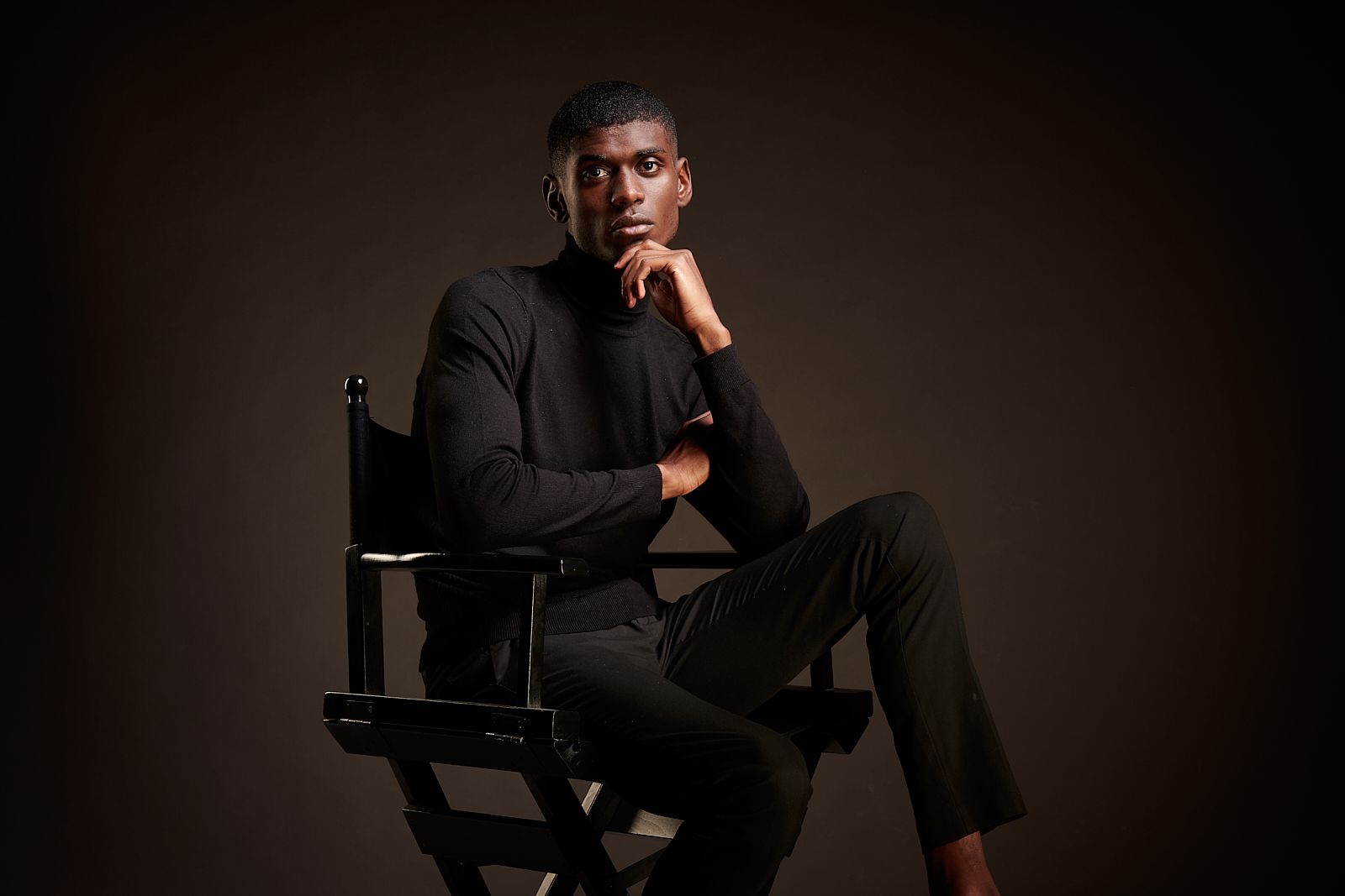 A man is sitting in a director 's chair with his hand on his chin.