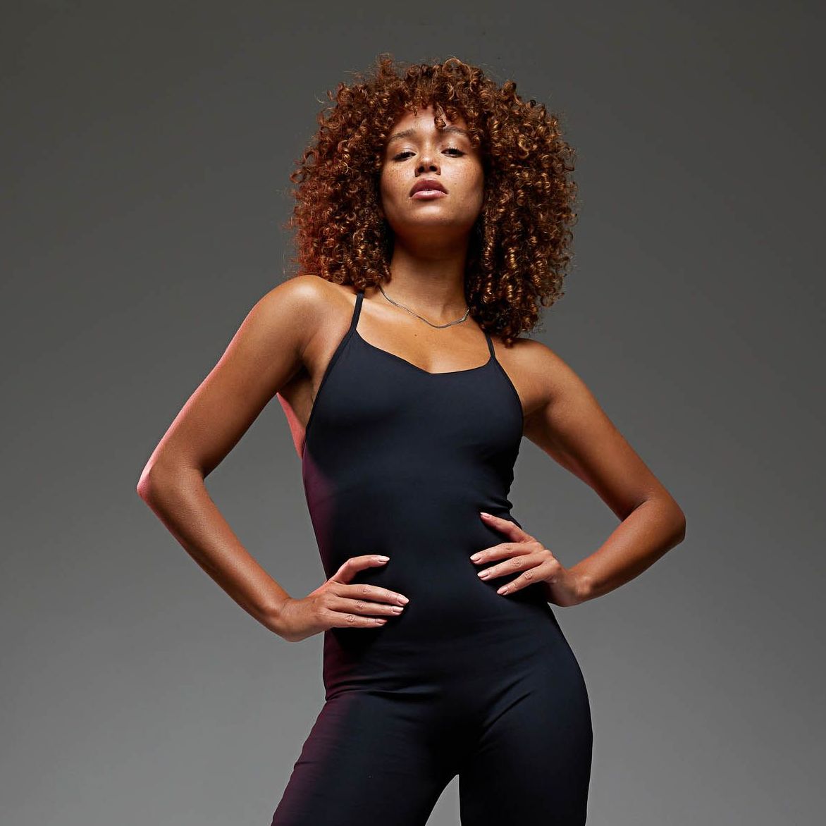 a woman with curly hair is wearing a black jumpsuit
