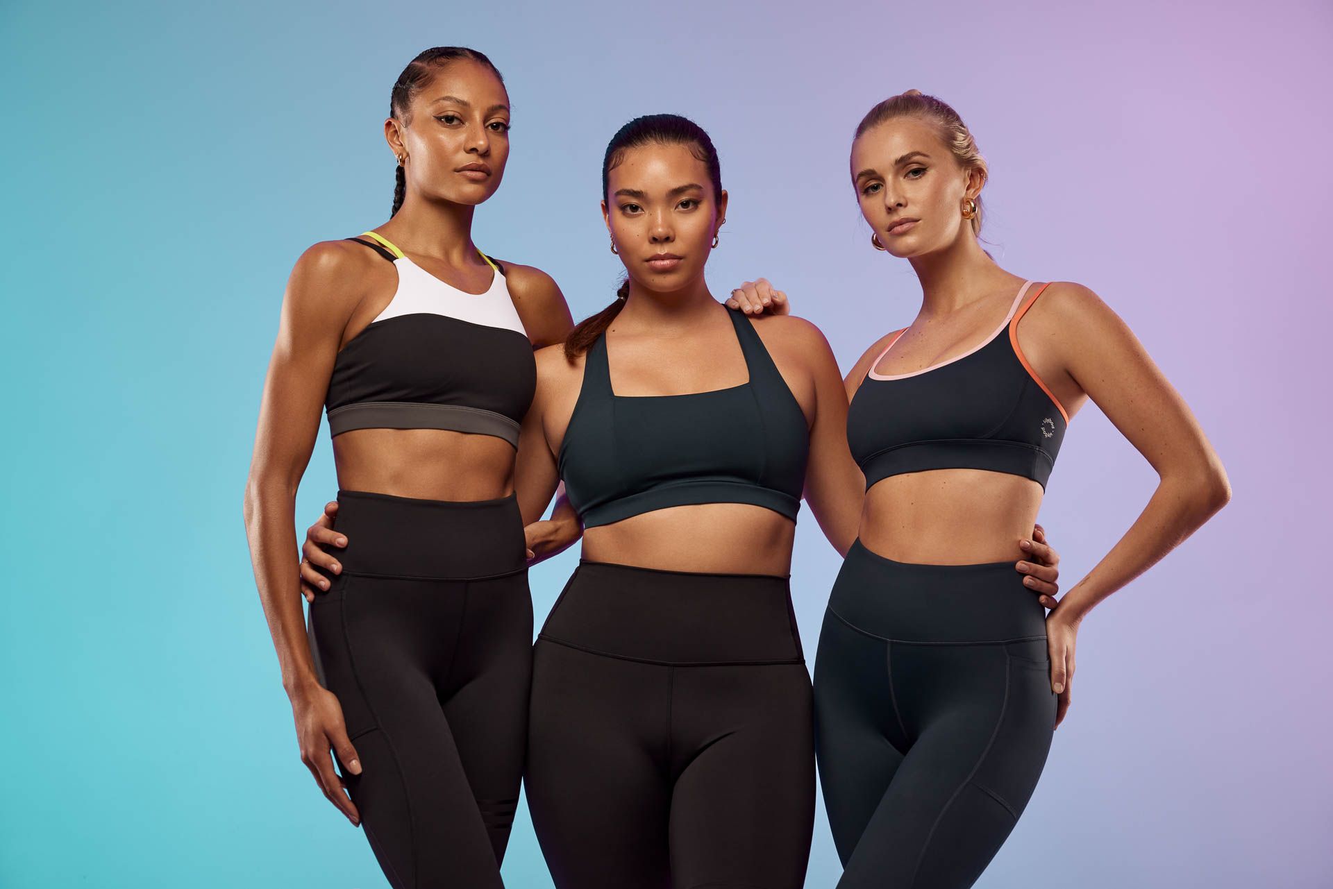 three women in sports bras and leggings are posing for a picture .