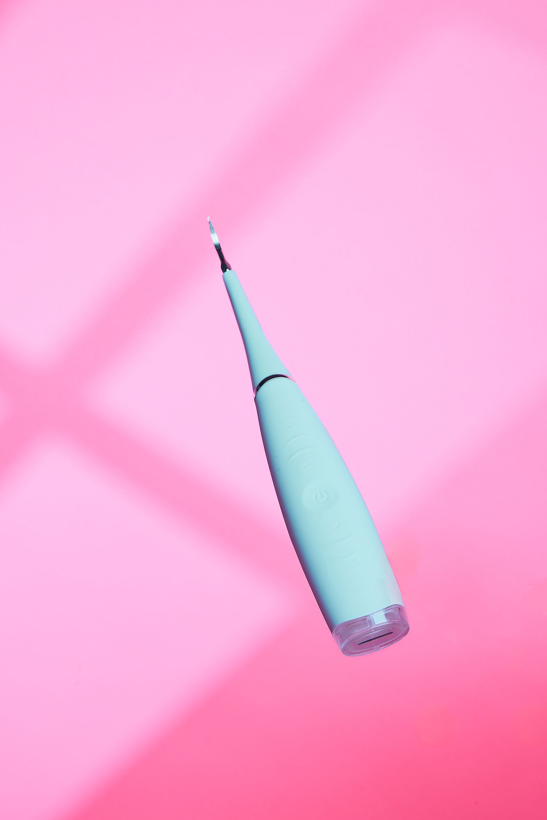 A blue tooth cleaner is floating in the air on a pink background.
