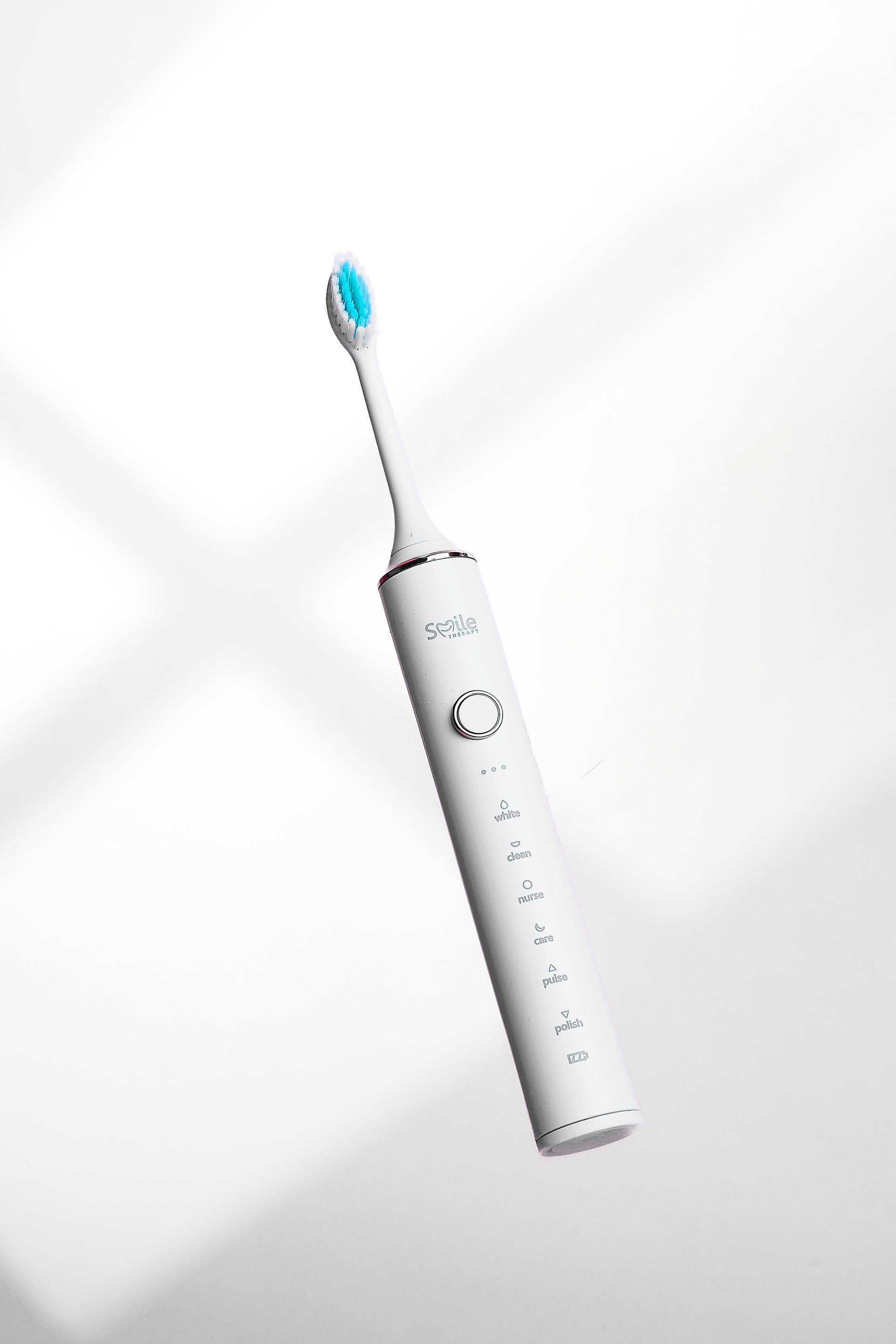 An electric toothbrush is floating in the air on a white surface.