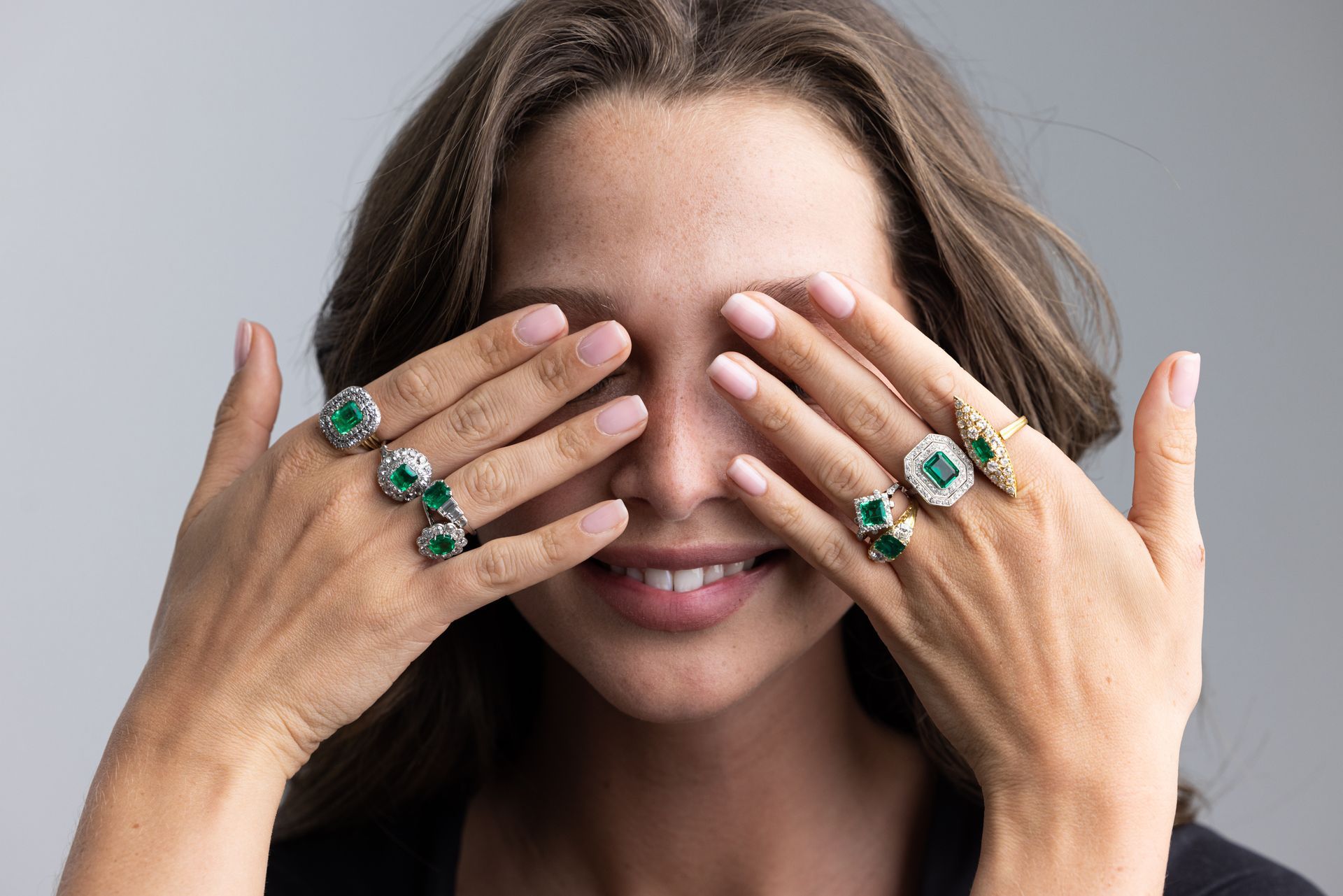 a woman is covering her eyes with her hands wearing rings .