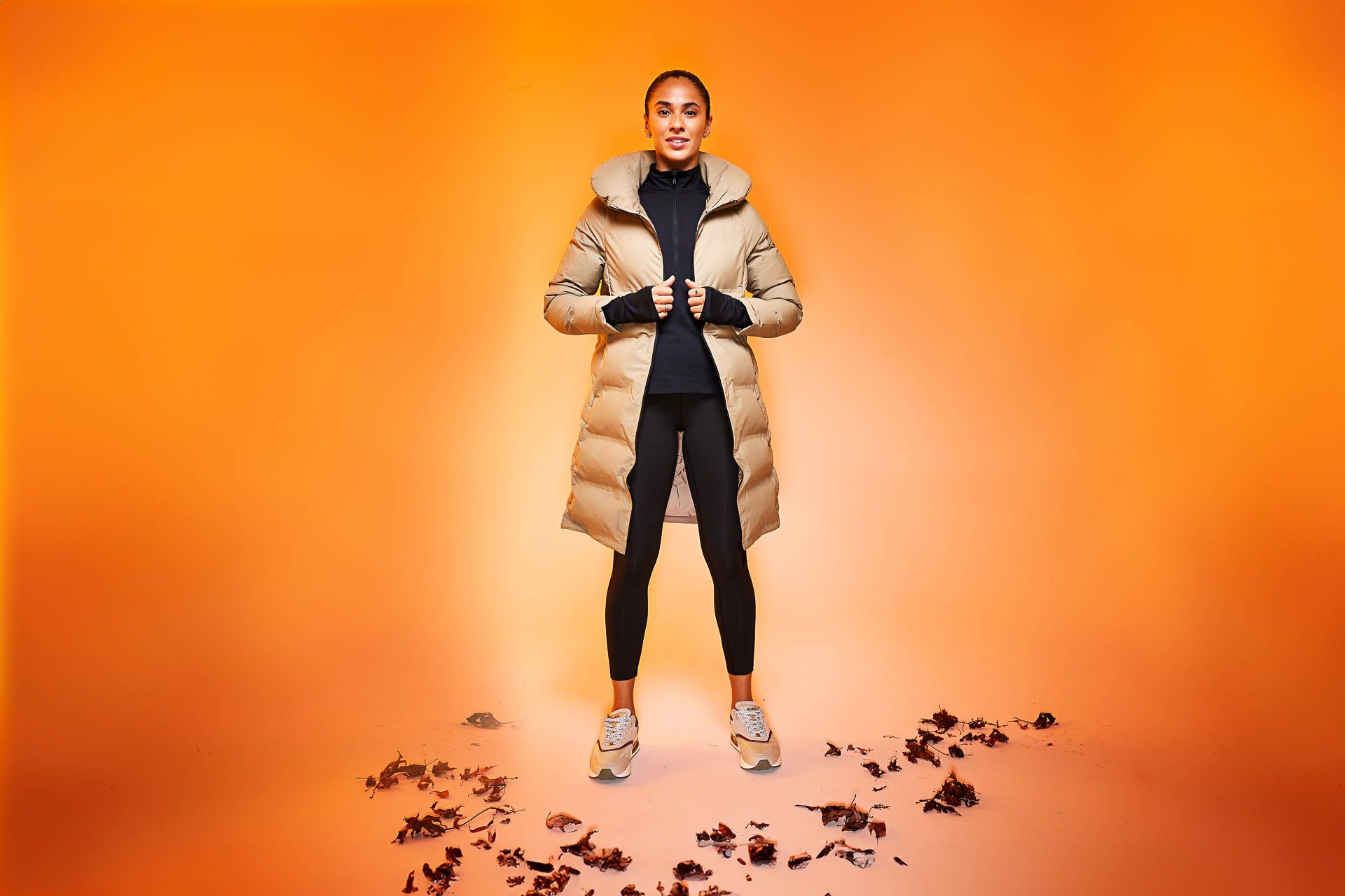 a woman in a long coat is standing in front of a pile of leaves .