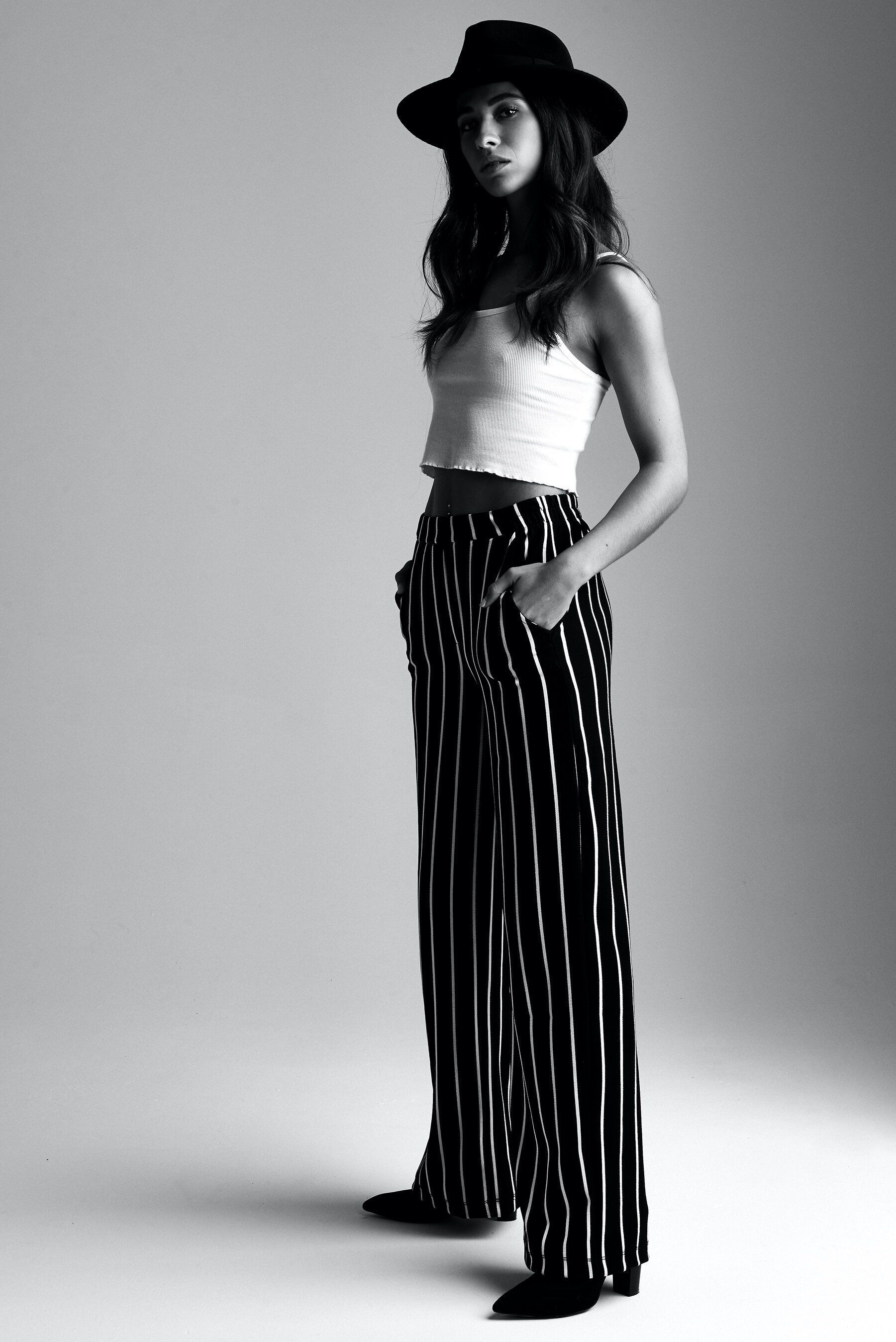 A black and white photo of a woman wearing a hat and striped pants