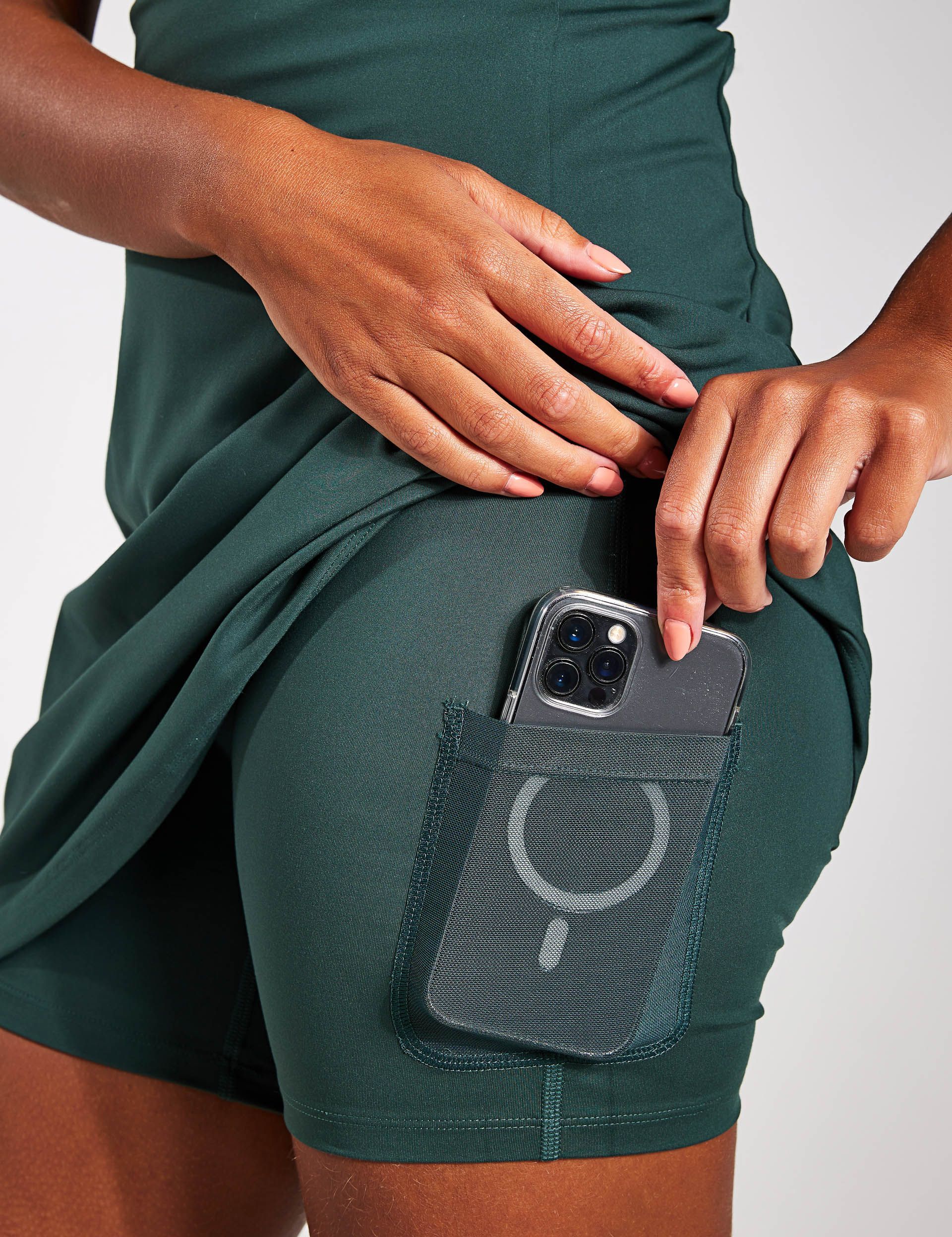 a woman in a green dress is holding a cell phone in her pocket .