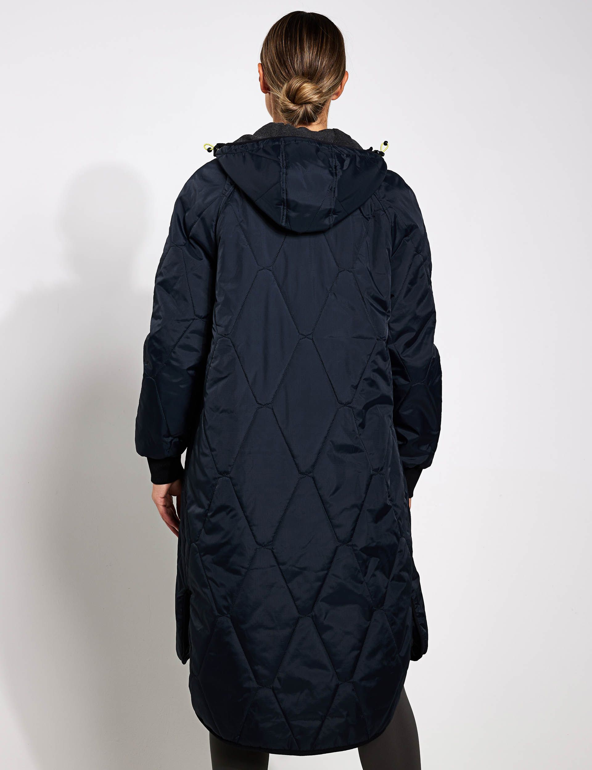 a woman is wearing a long quilted coat with a hood