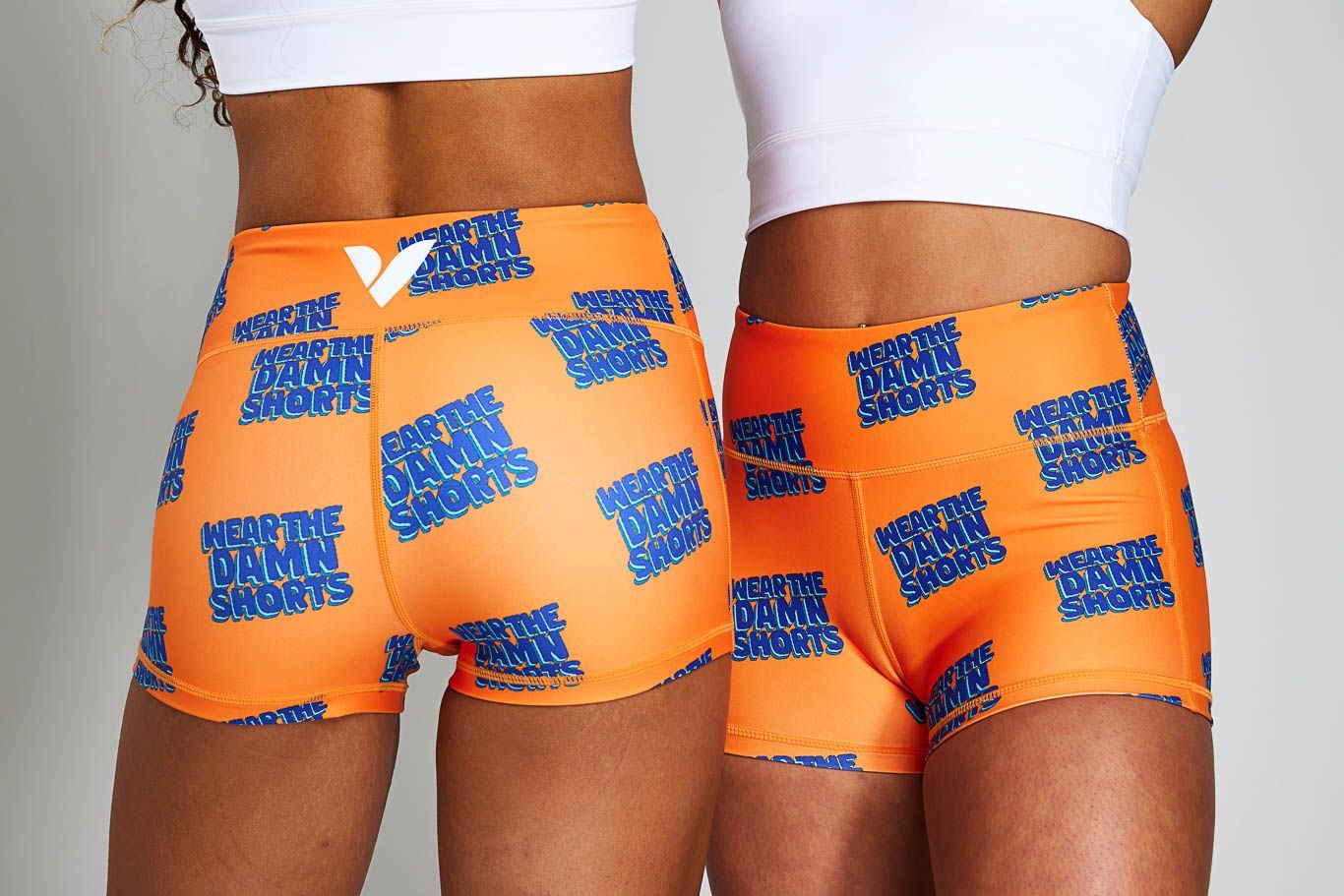 two women wearing orange shorts with blue writing on them
