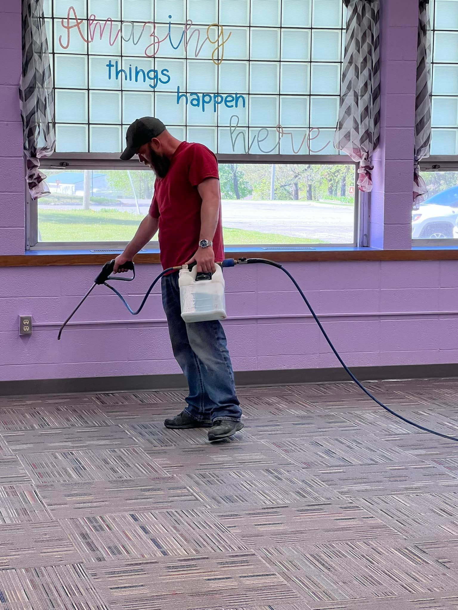 A man is spraying a carpet with a sprayer in a room.