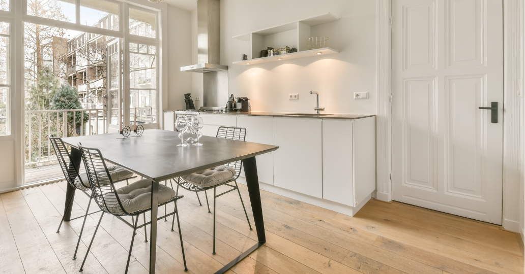Modern kitchen with a dining table and chairs, natural light from a window, and white cabinetry.