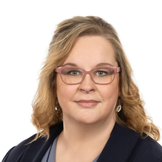 Woman wearing glasses and blazer, smiling, headshot against white background.