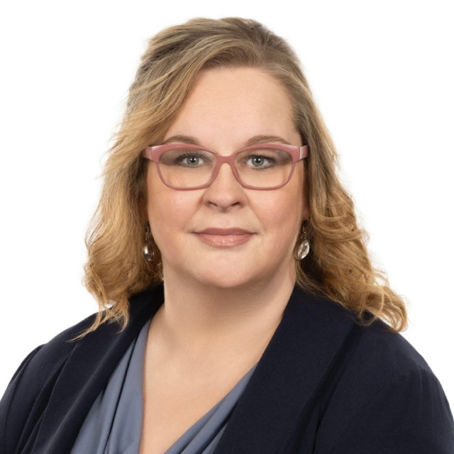 Woman with blond hair, glasses, and a blue blazer smiles at the camera.