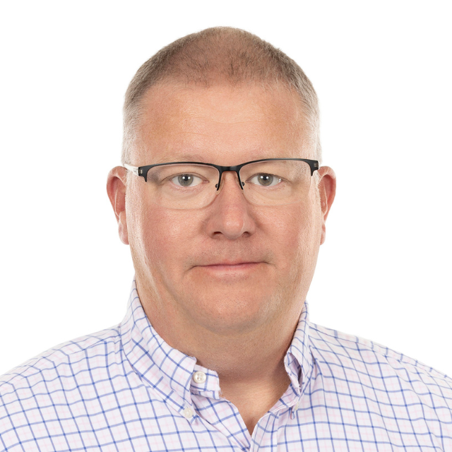 Man wearing glasses and a plaid shirt, smiling in front of a white background.