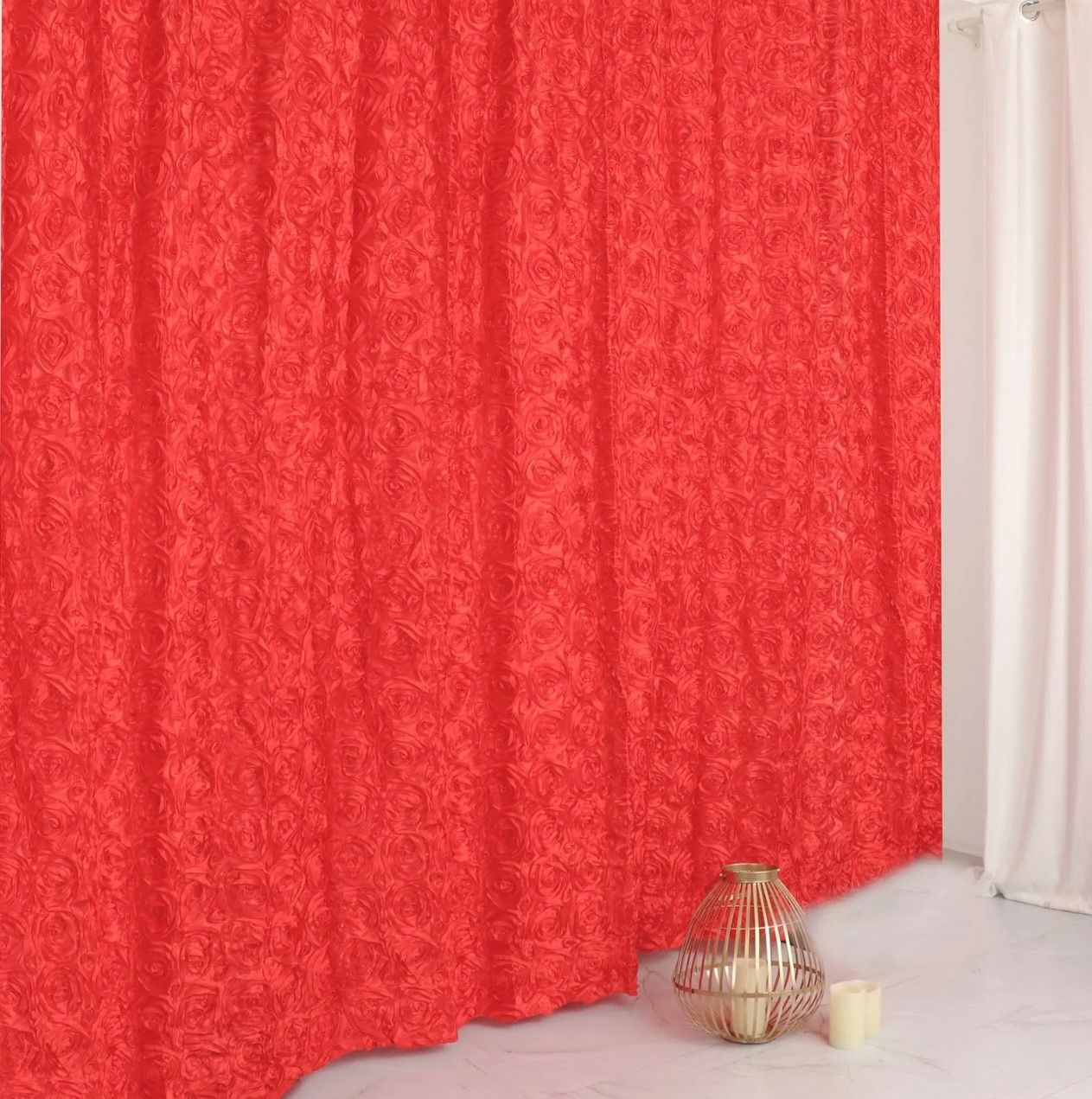 A red curtain is hanging on a window next to a bird cage and candles.