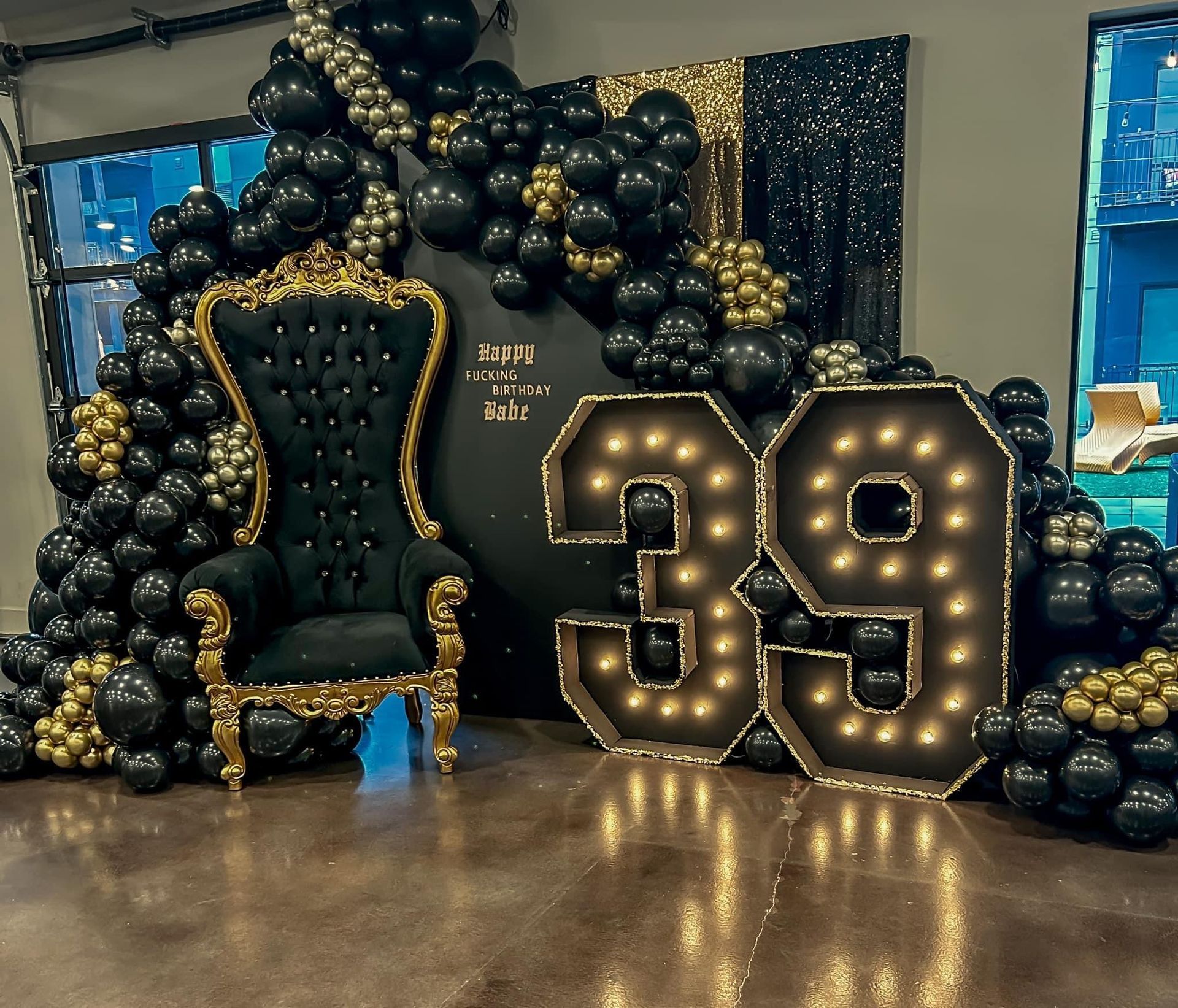 A chair is surrounded by black and gold balloons and a large number 39.