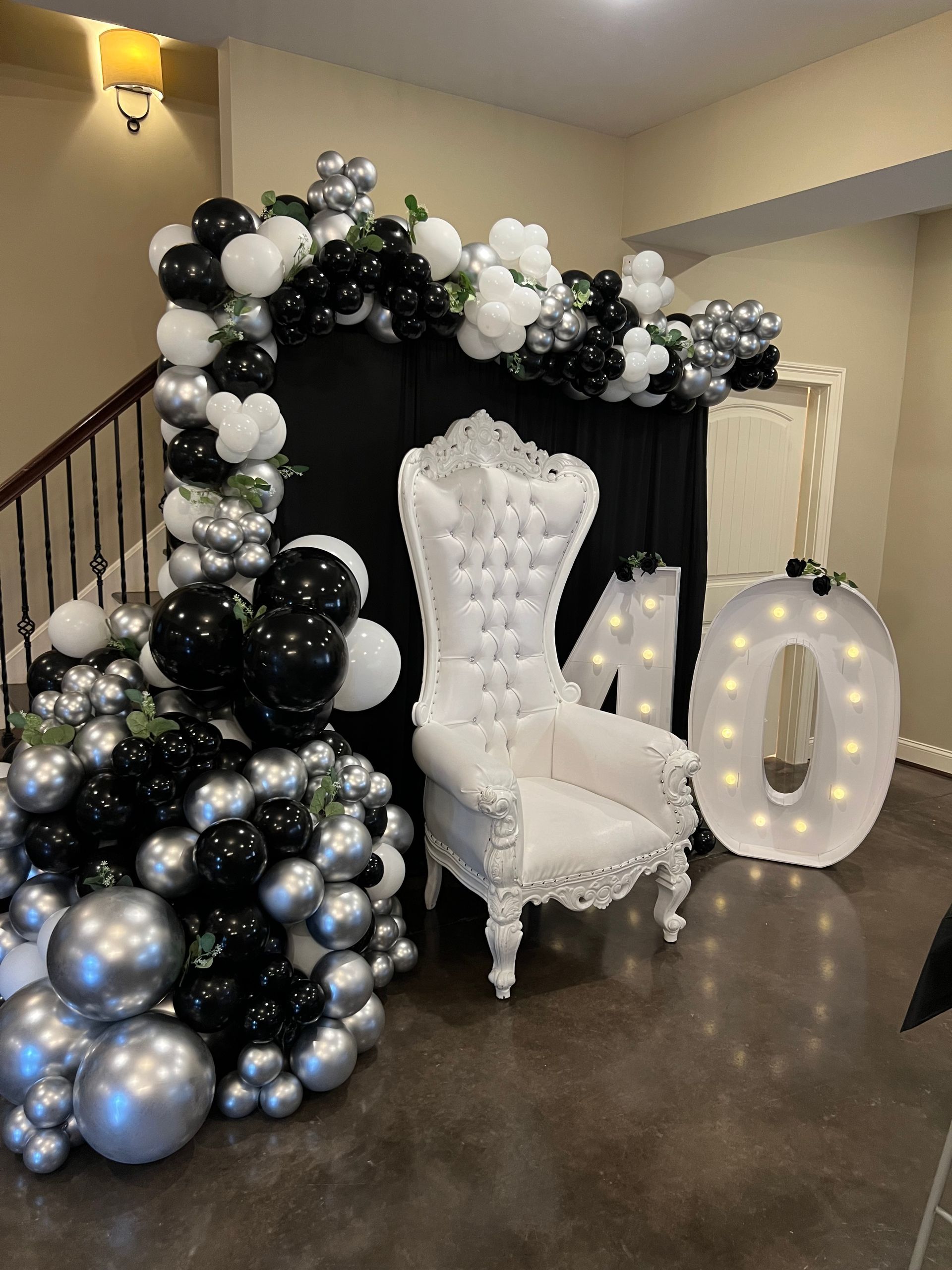 A white chair is surrounded by black and silver balloons.