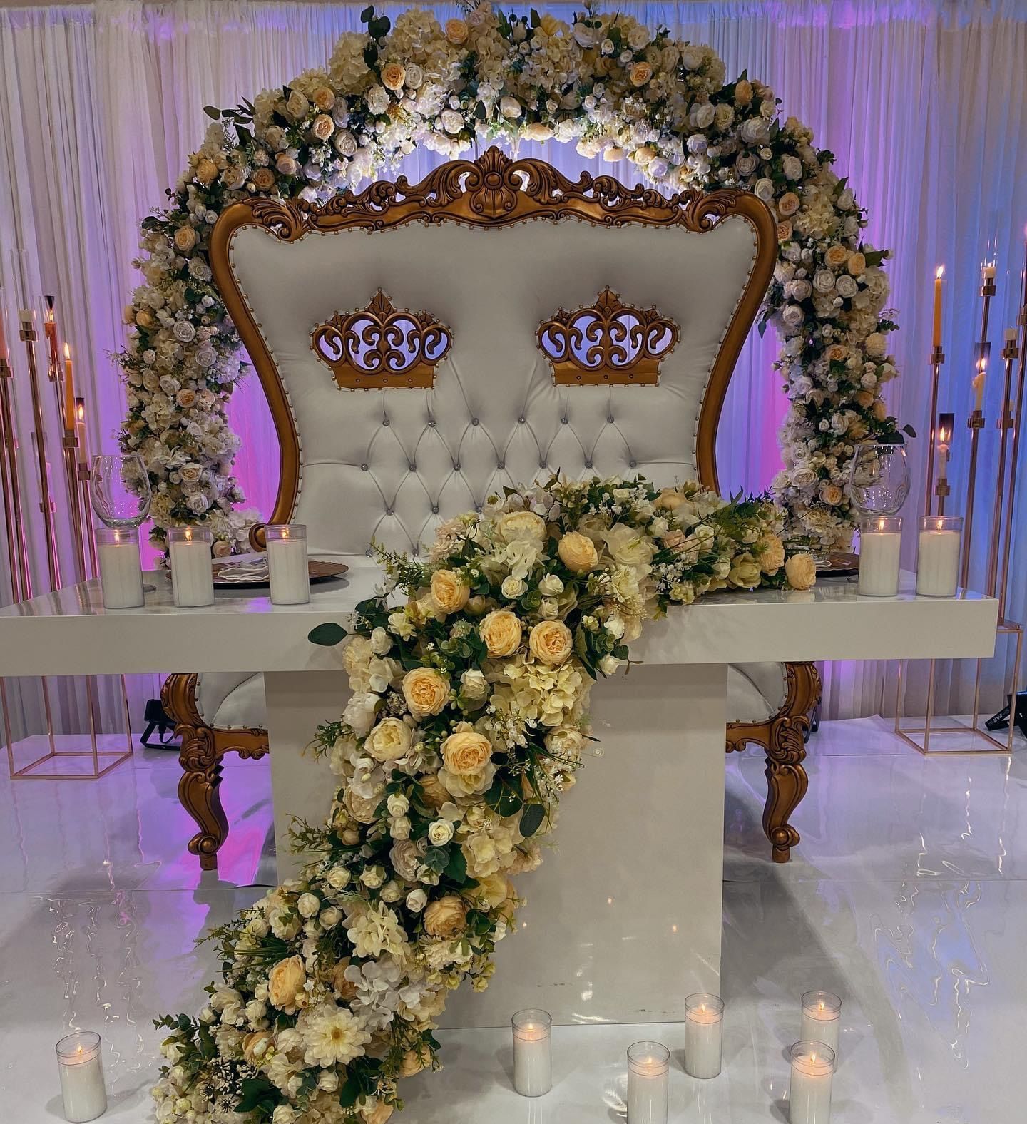 A throne with a crown on it is surrounded by flowers and candles.