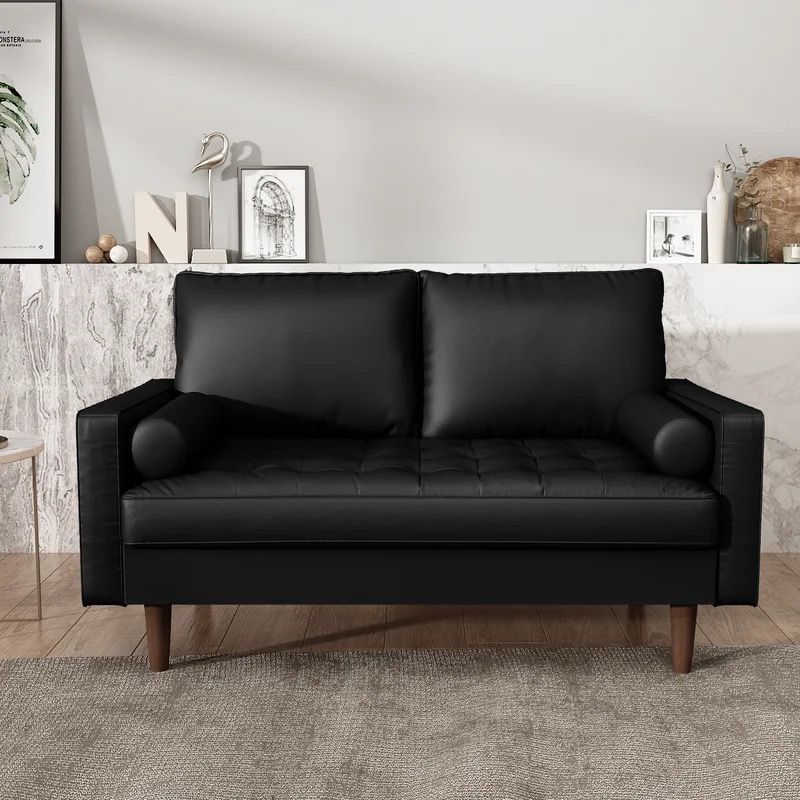 A black leather couch is sitting on a rug in a living room.