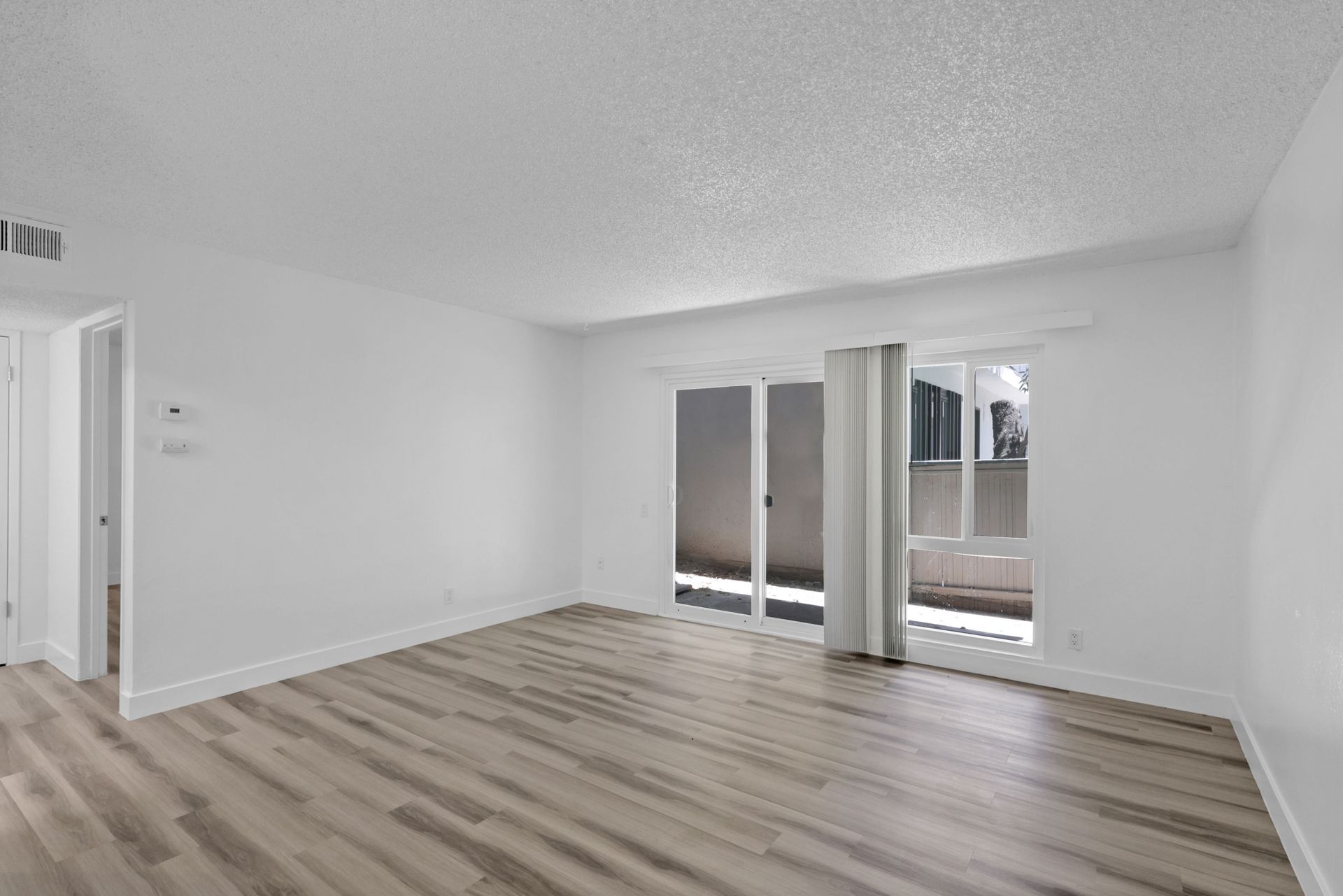 An empty living room with hardwood floors and sliding glass doors.