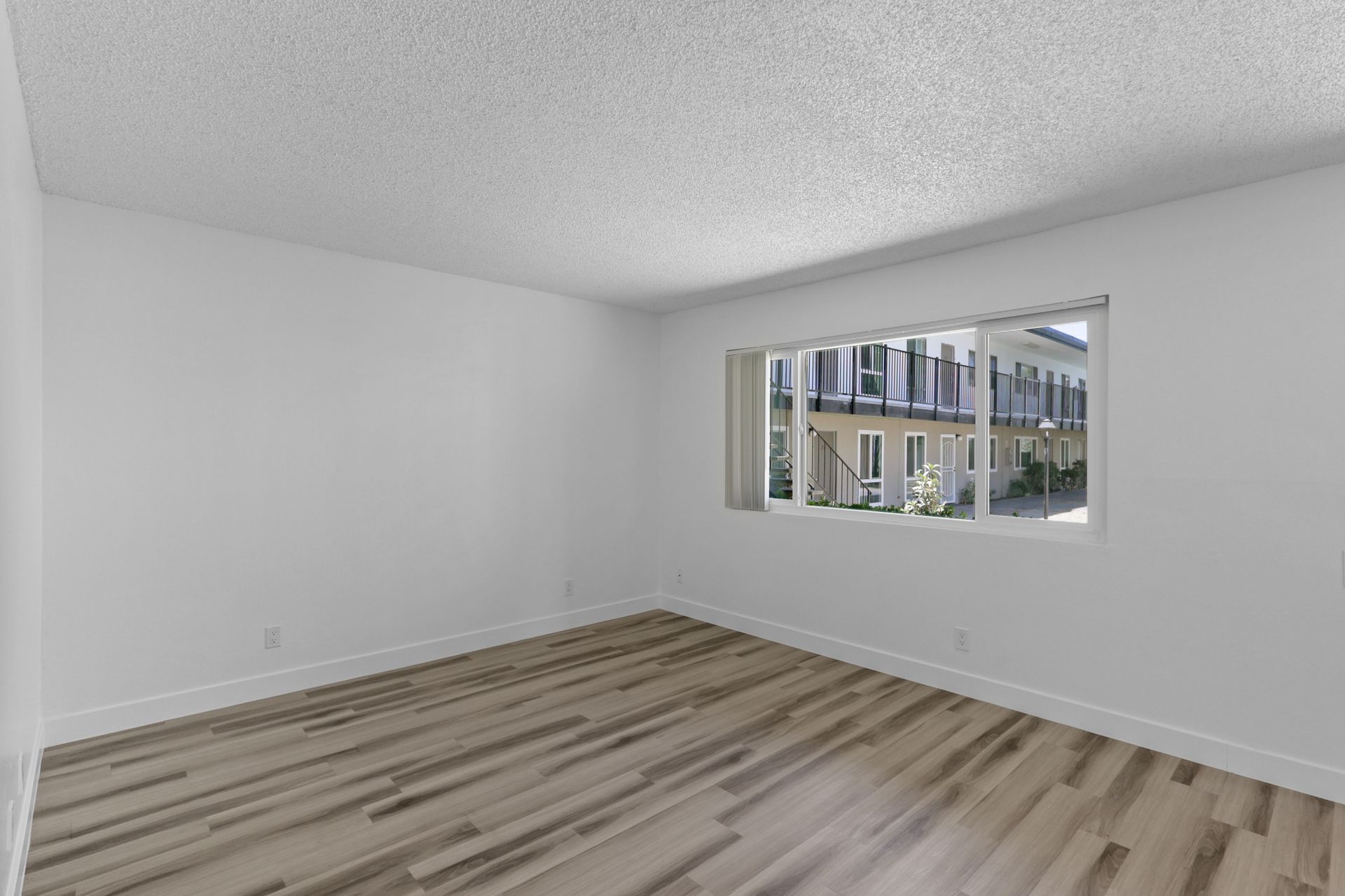 An empty living room with hardwood floors and a large window.