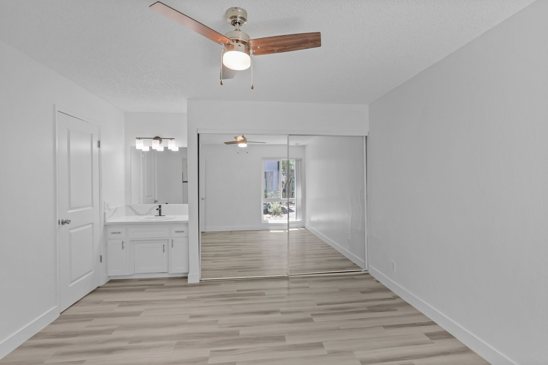 An empty room with a ceiling fan and a mirror.