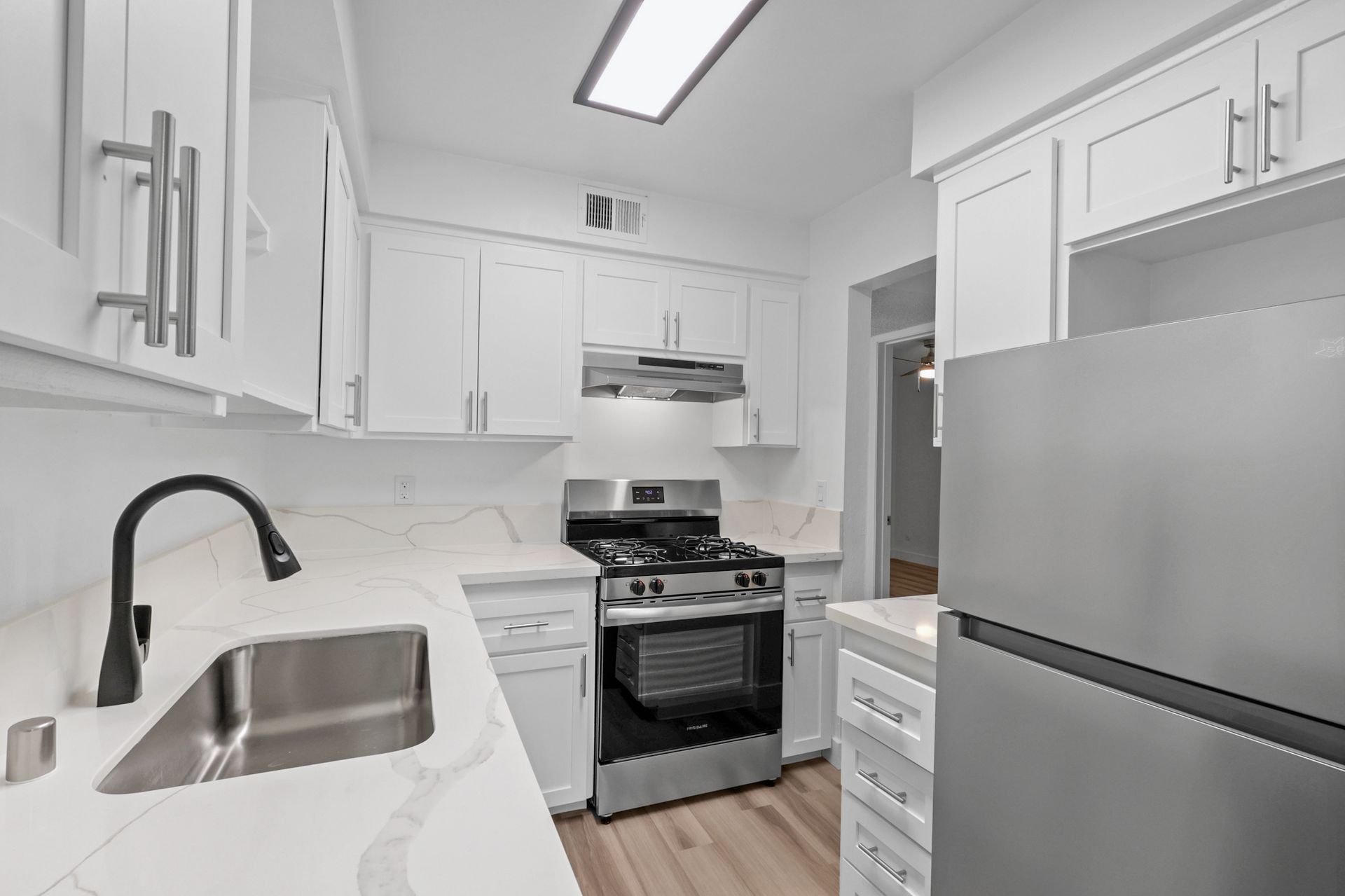 A kitchen with white cabinets , stainless steel appliances , a sink , and a refrigerator.