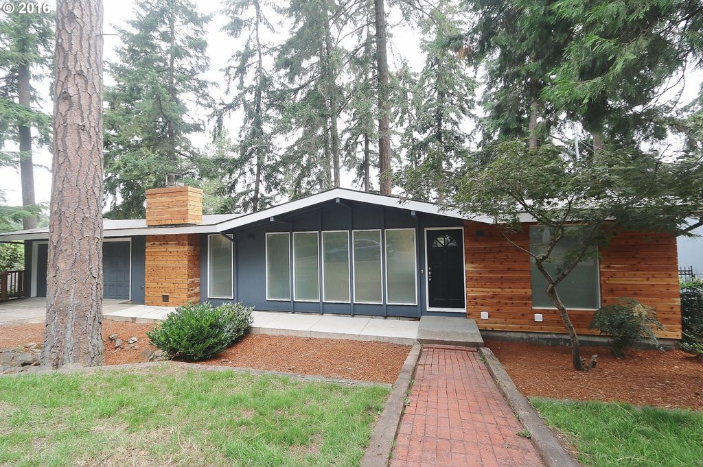 A house with a brick walkway leading to it is surrounded by trees.