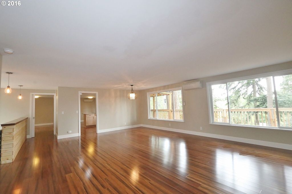 An empty living room with hardwood floors and lots of windows.