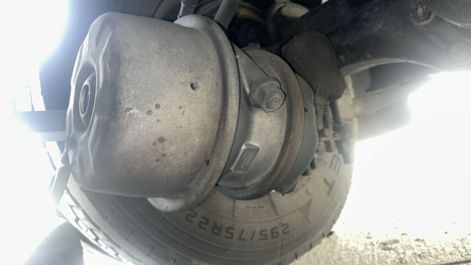 Close-up of a truck’s wheel hub and tire underside, dusty and partially backlit by bright sunlight