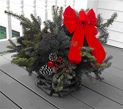 Christmas evergreen arrangement with a red bow, pinecones, and berries on a porch.