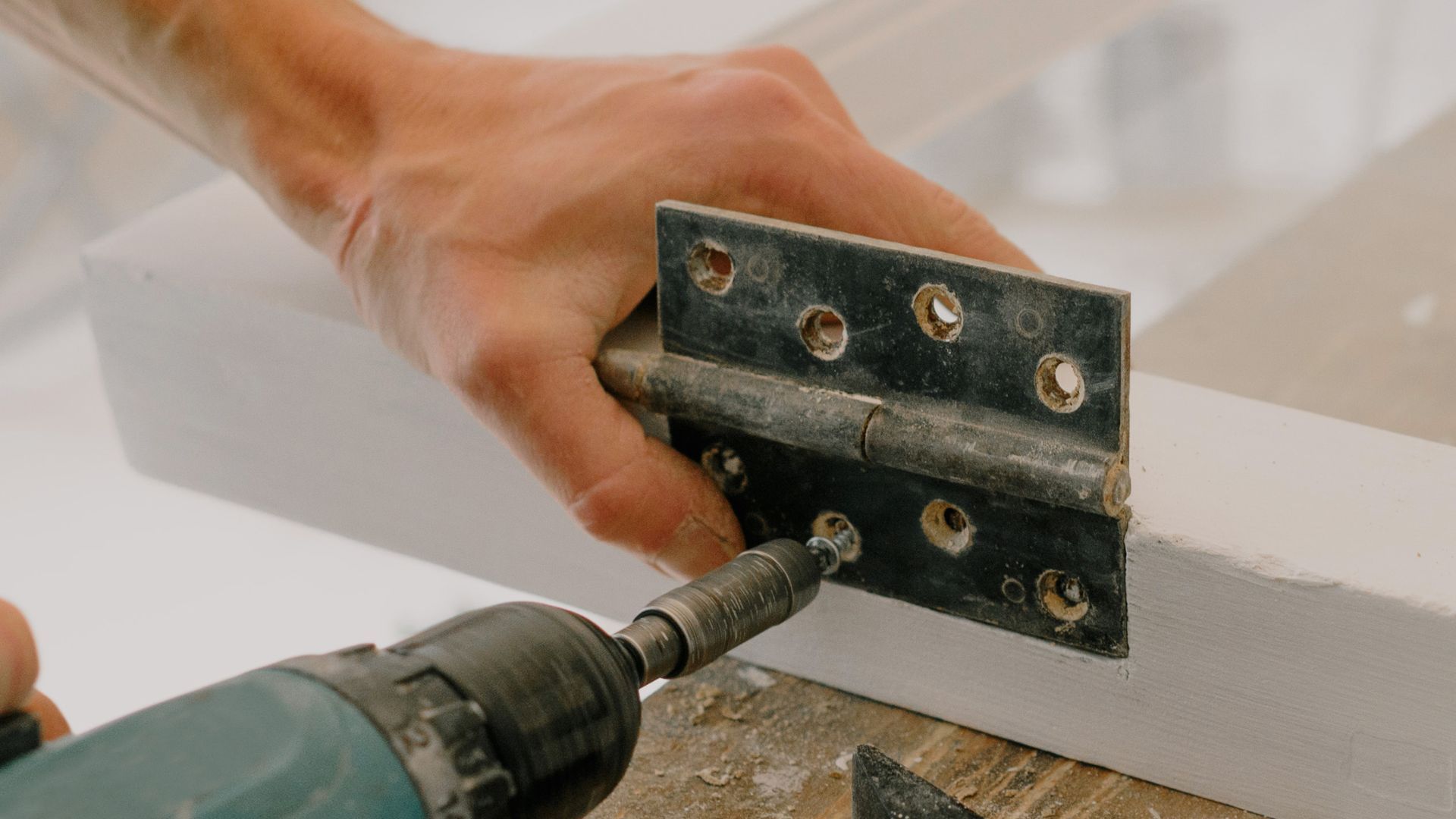 A person is using a drill to fix a door hinge.