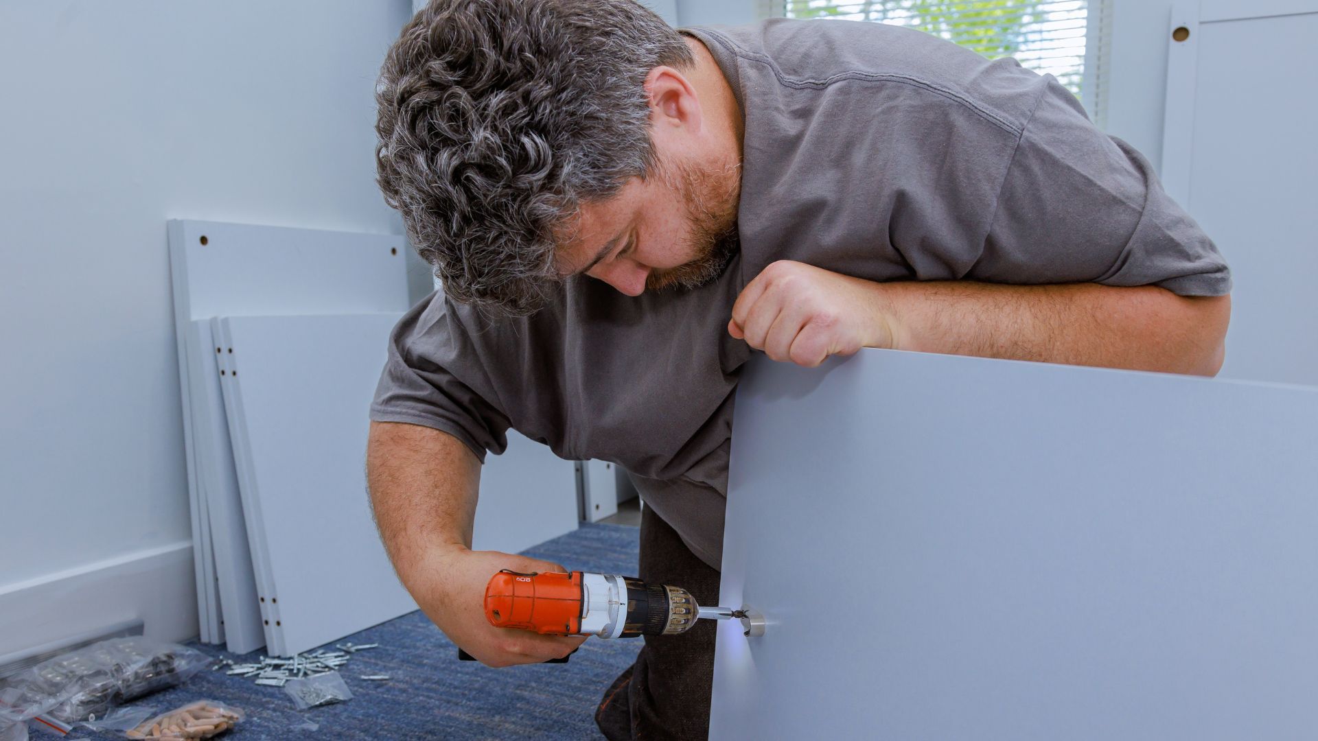 A man is using a drill to fix a piece of furniture.