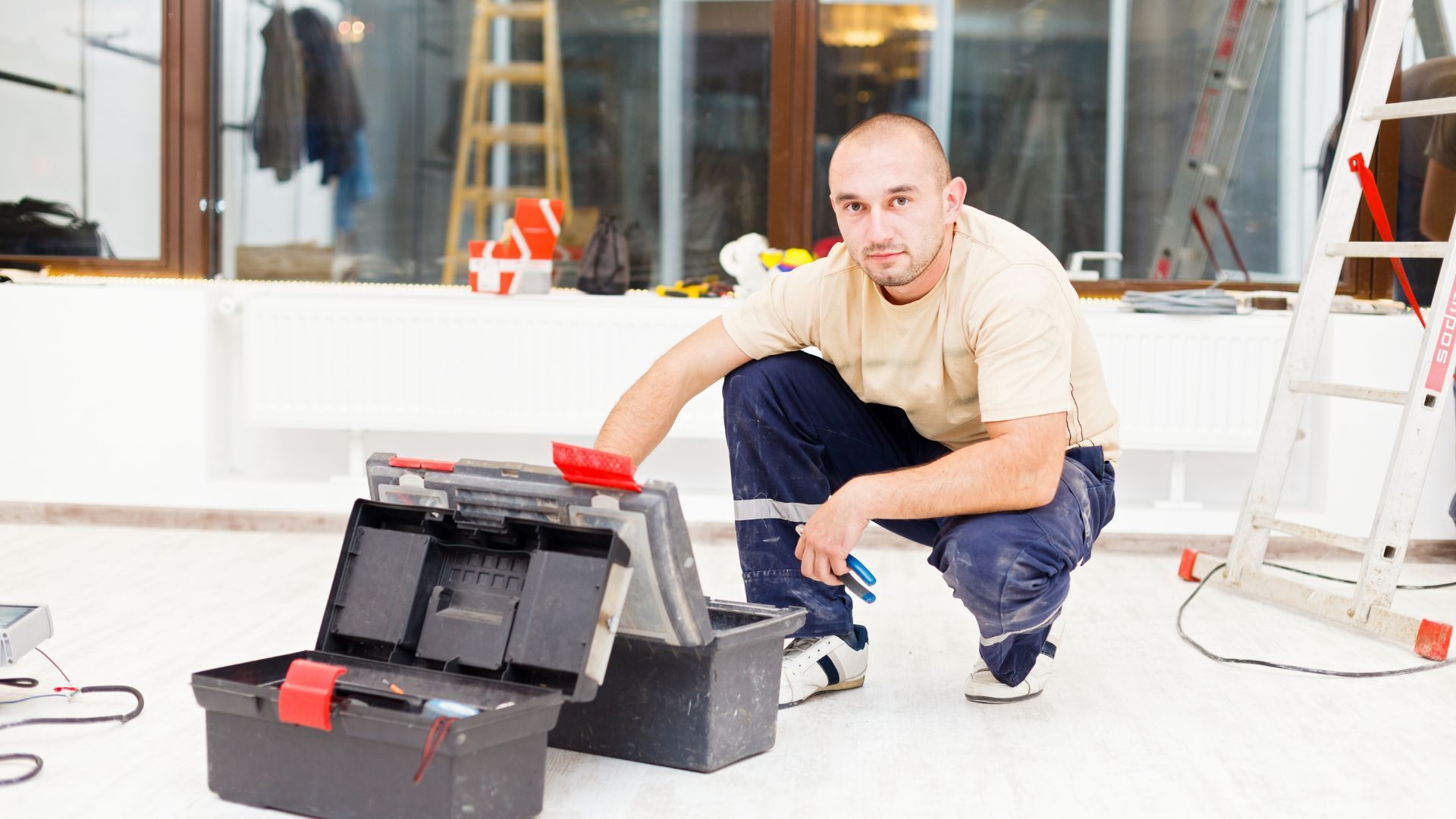 A man is kneeling down next to a toolbox in a room.