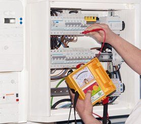 A person is working on an electrical box with a yellow device.
