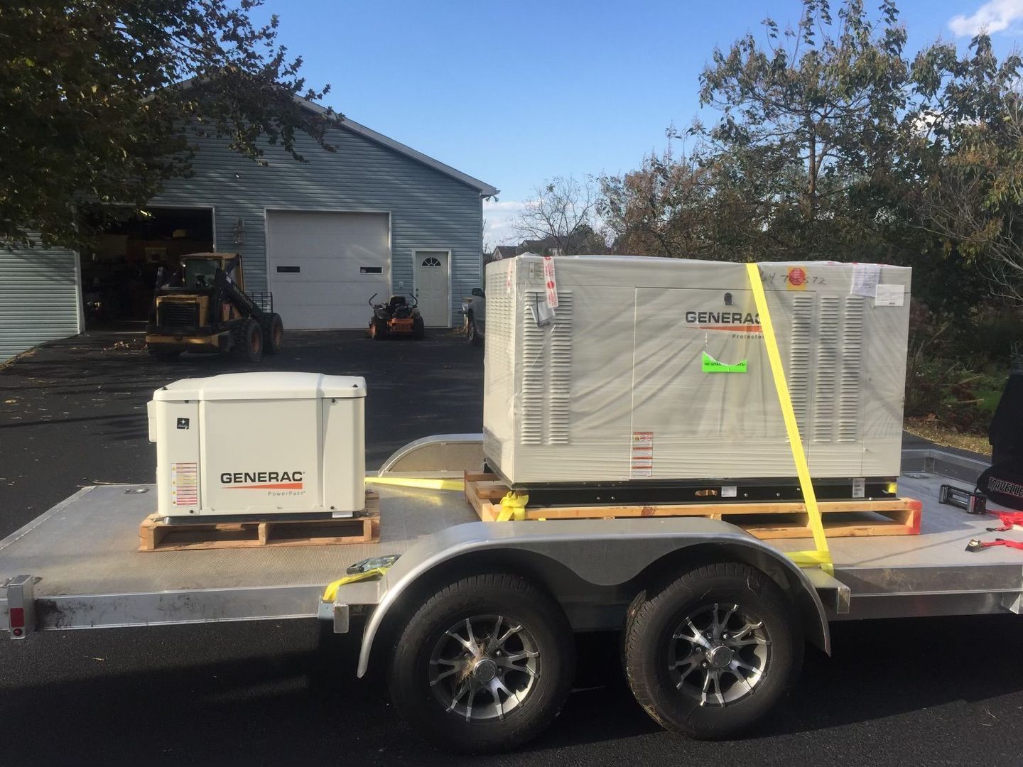 A generator is sitting on top of a trailer in front of a garage.