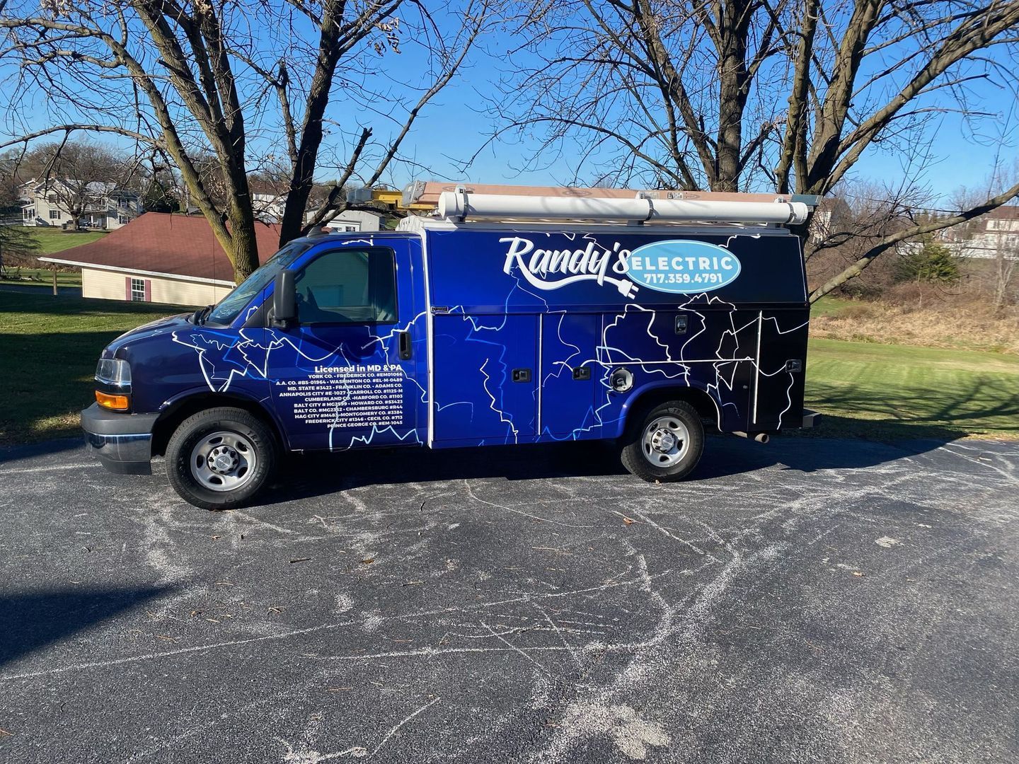Blue utility van with "Randy's Electric" logo, parked on pavement with trees and houses in the background.