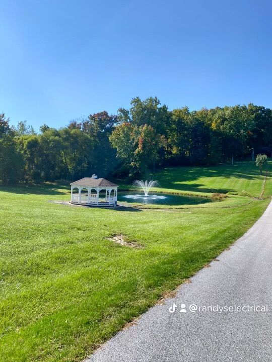 A white gazebo is sitting in the middle of a grassy field next to a fountain.