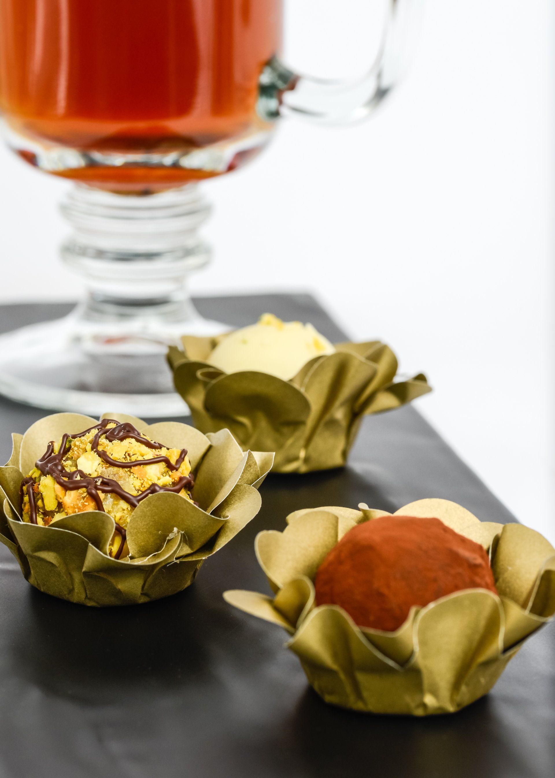 Three desserts are sitting on a table next to a glass of tea.