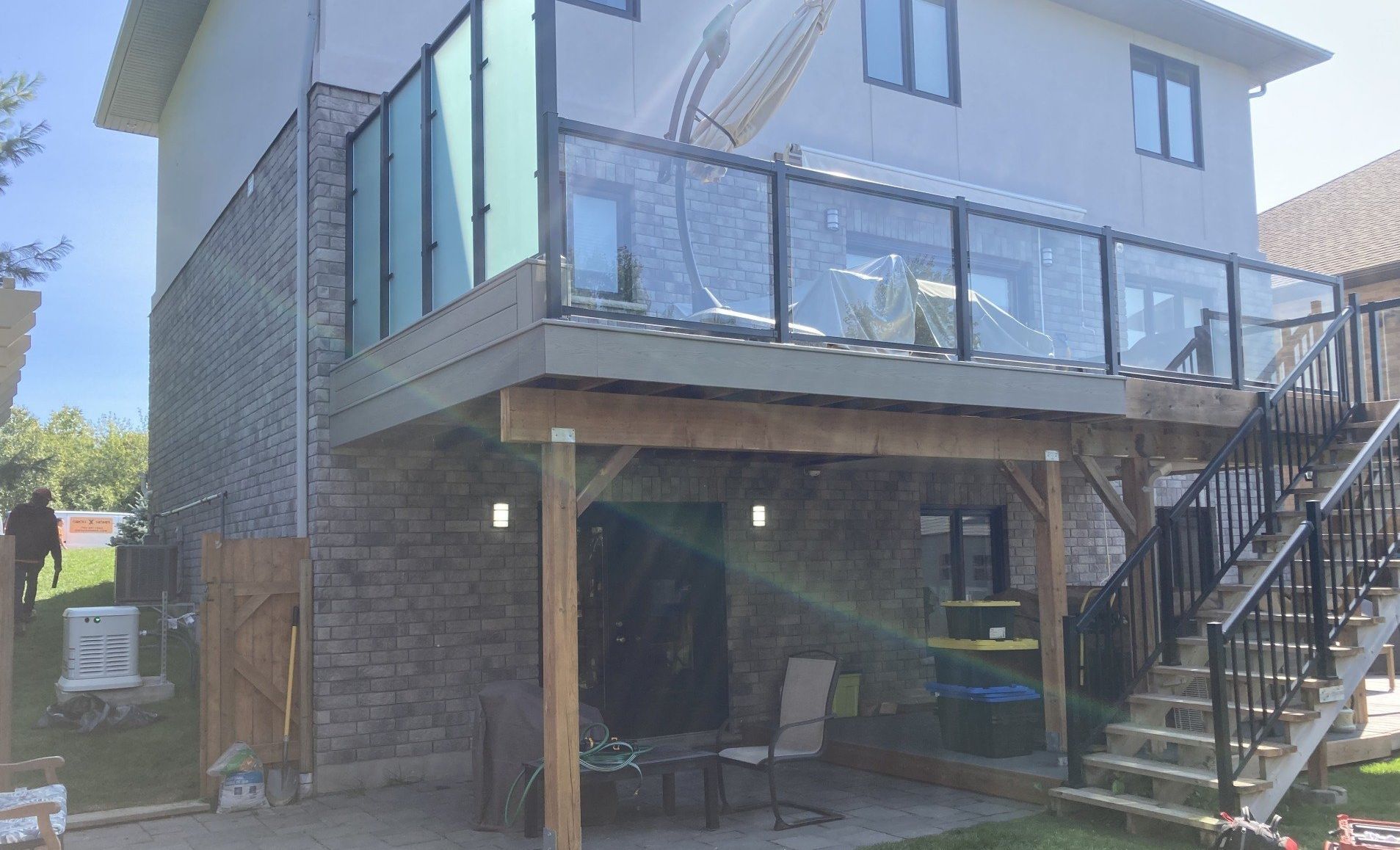 Backyard with a multi-level deck, glass railings, and a staircase. A patio with seating underneath.