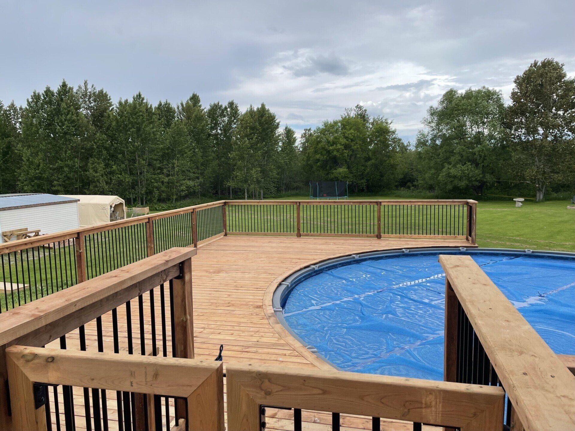 A wooden deck overlooking a swimming pool with a blue tarp on it.