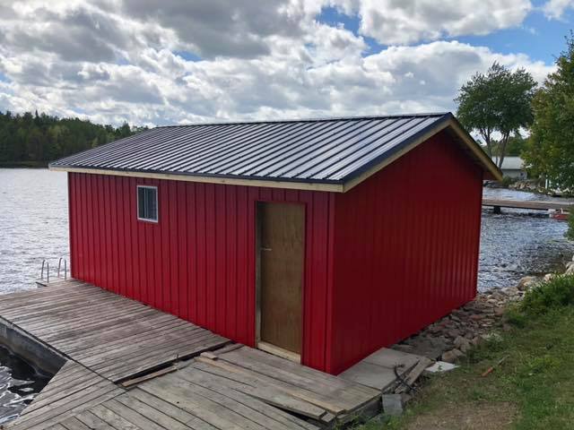 A red shed with a black roof is sitting next to a lake.
