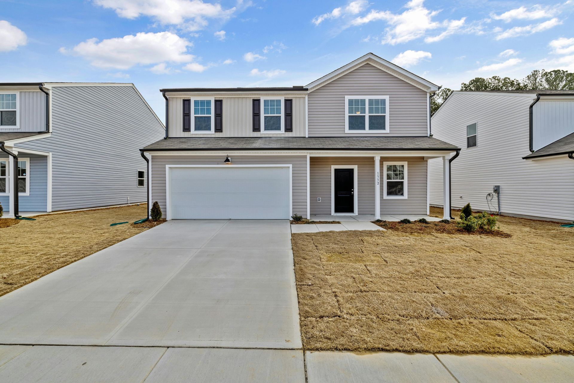 Two-story gray house with a two-car garage, blue sky, and dry grass yard.