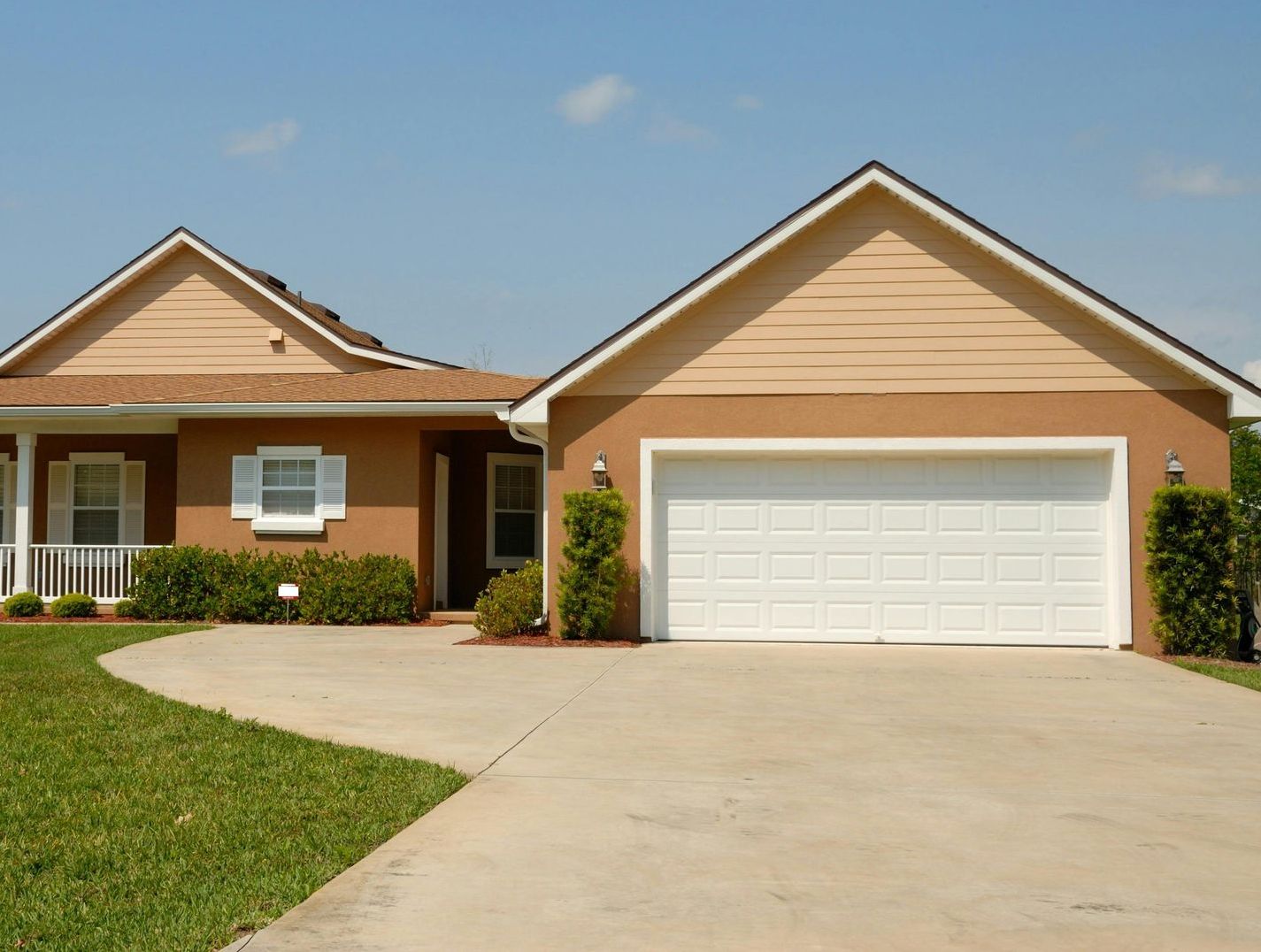 Tan suburban house with a driveway, garage, and green lawn under a blue sky.