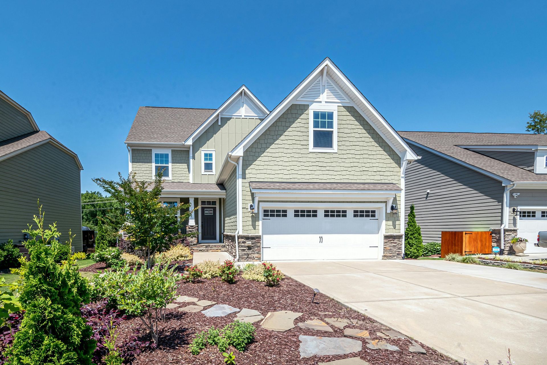 Two-story house with green siding, white garage door, and a blue sky.