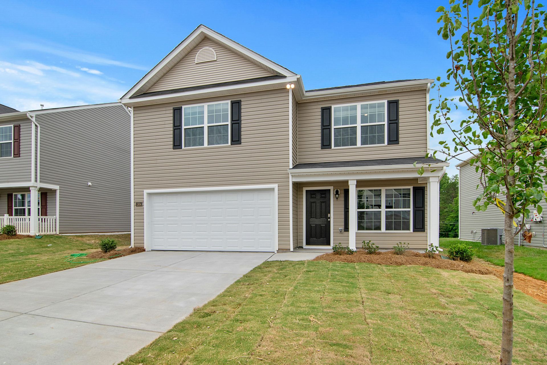 Two-story beige house with black shutters and a white garage door, set against a blue sky.