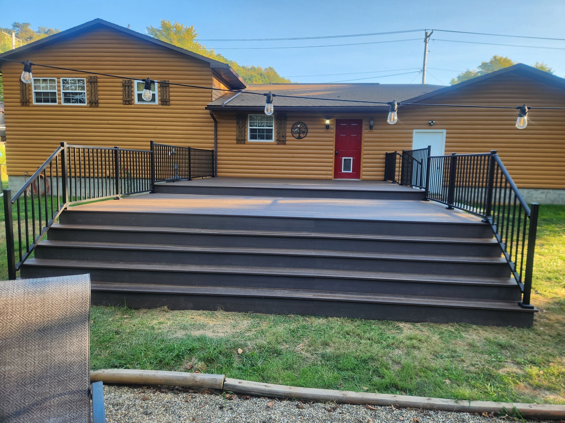 A log-sided house featuring a wide, multi-step dark deck with black metal railings and a red front door.