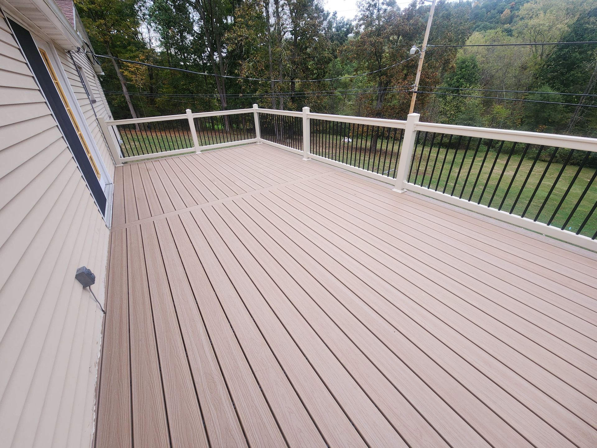 An elevated outdoor composite deck with light brown boards and white railings with black balusters, overlooking a yard.