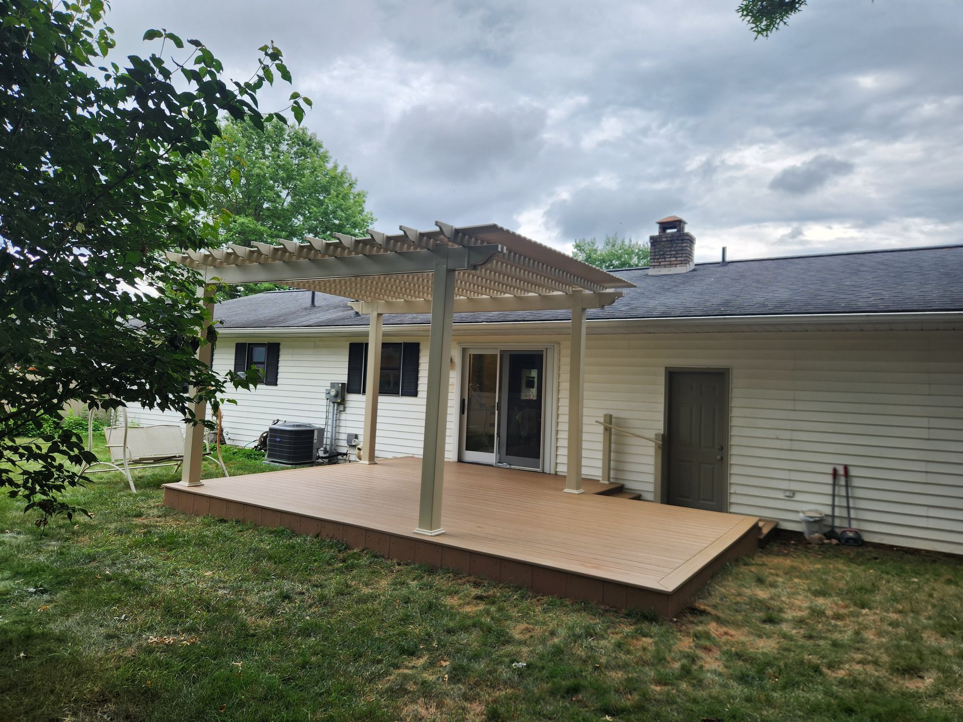 A newly built wooden pergola stands over a tan composite deck attached to the rear of a white-sided house.
