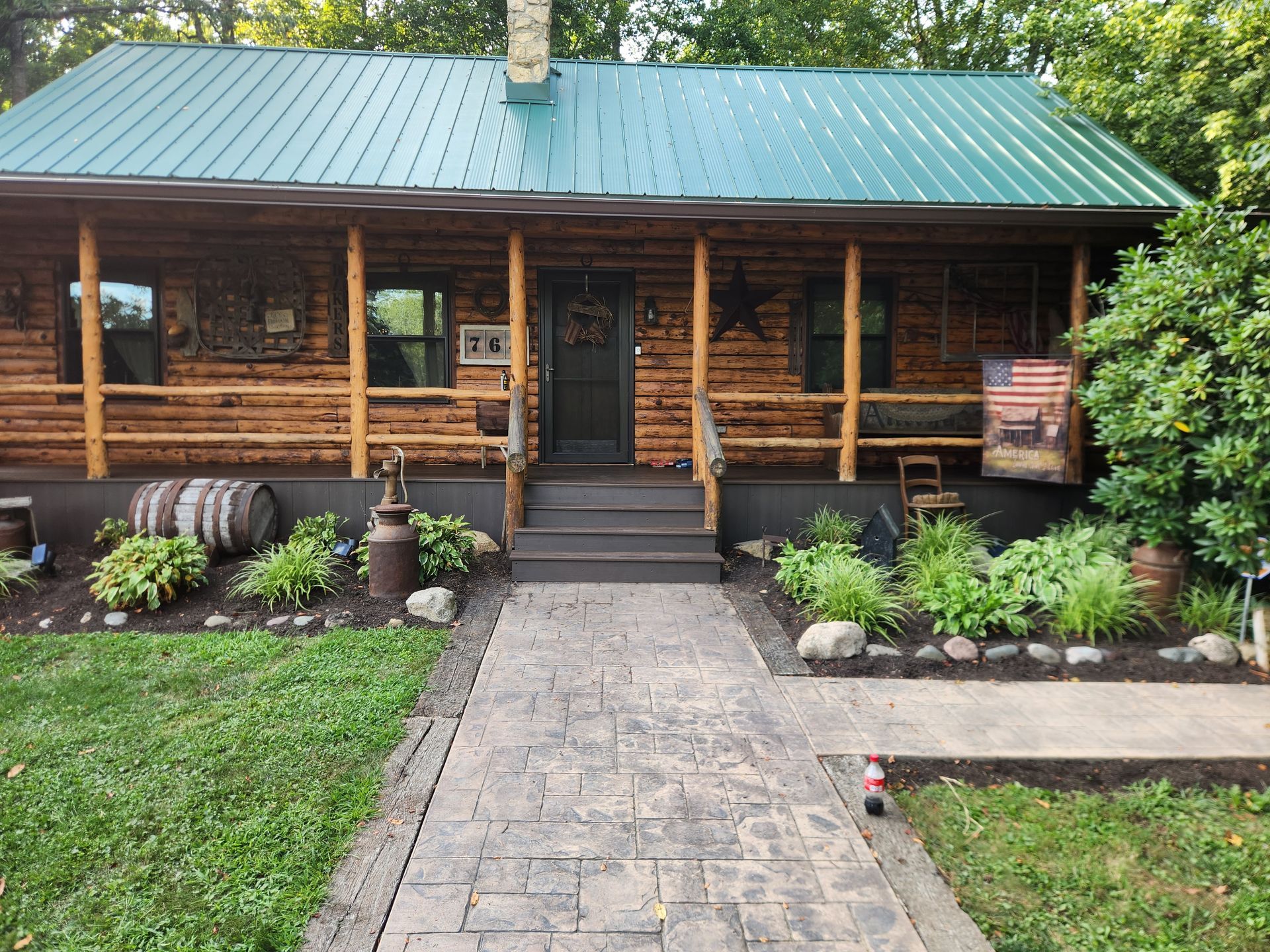 A rustic log cabin with a green metal roof, a front porch, and a stone walkway leading to the entrance.