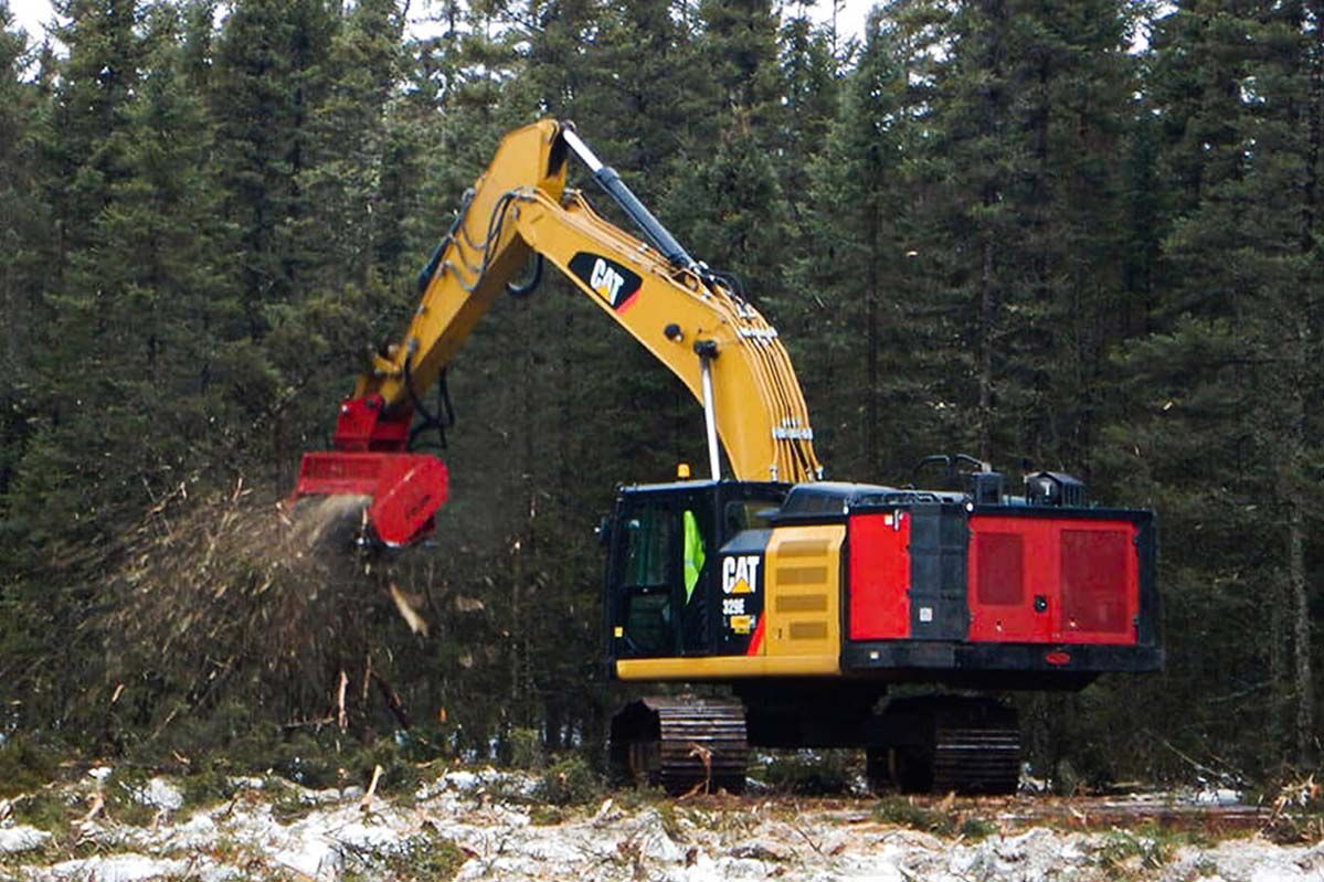 Yellow and red Caterpillar machine mulching brush in a forest, with snow on the ground.