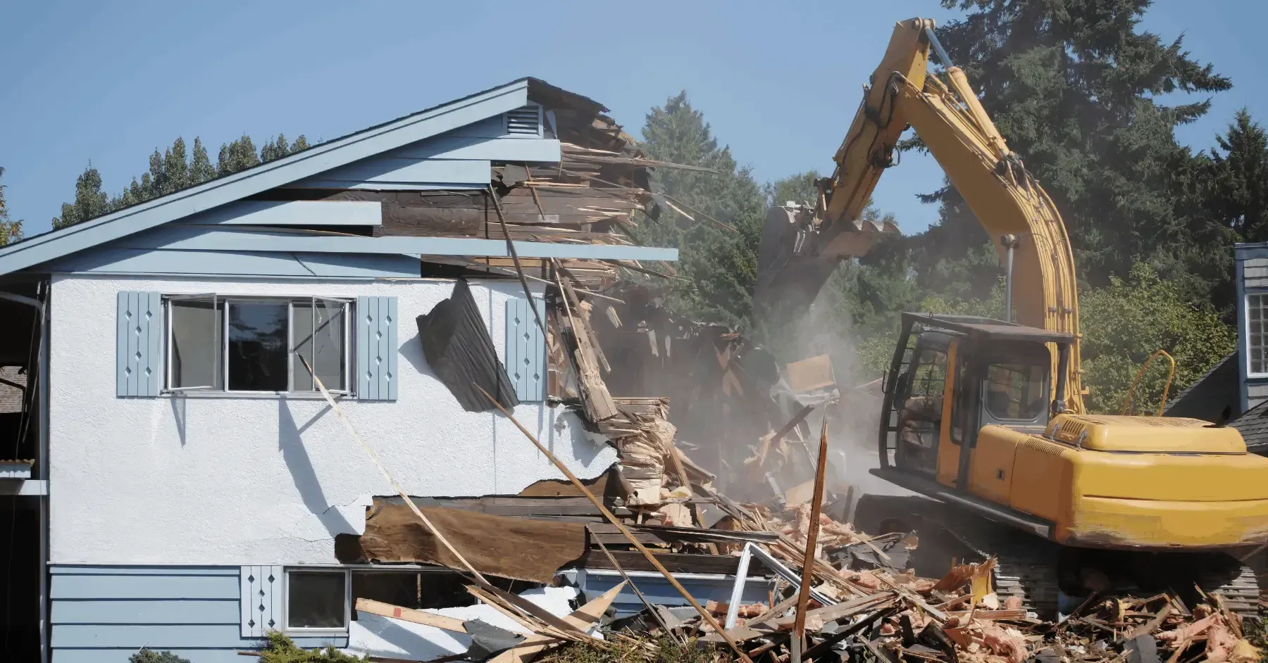 Yellow excavator demolishing a house on a sunny day.